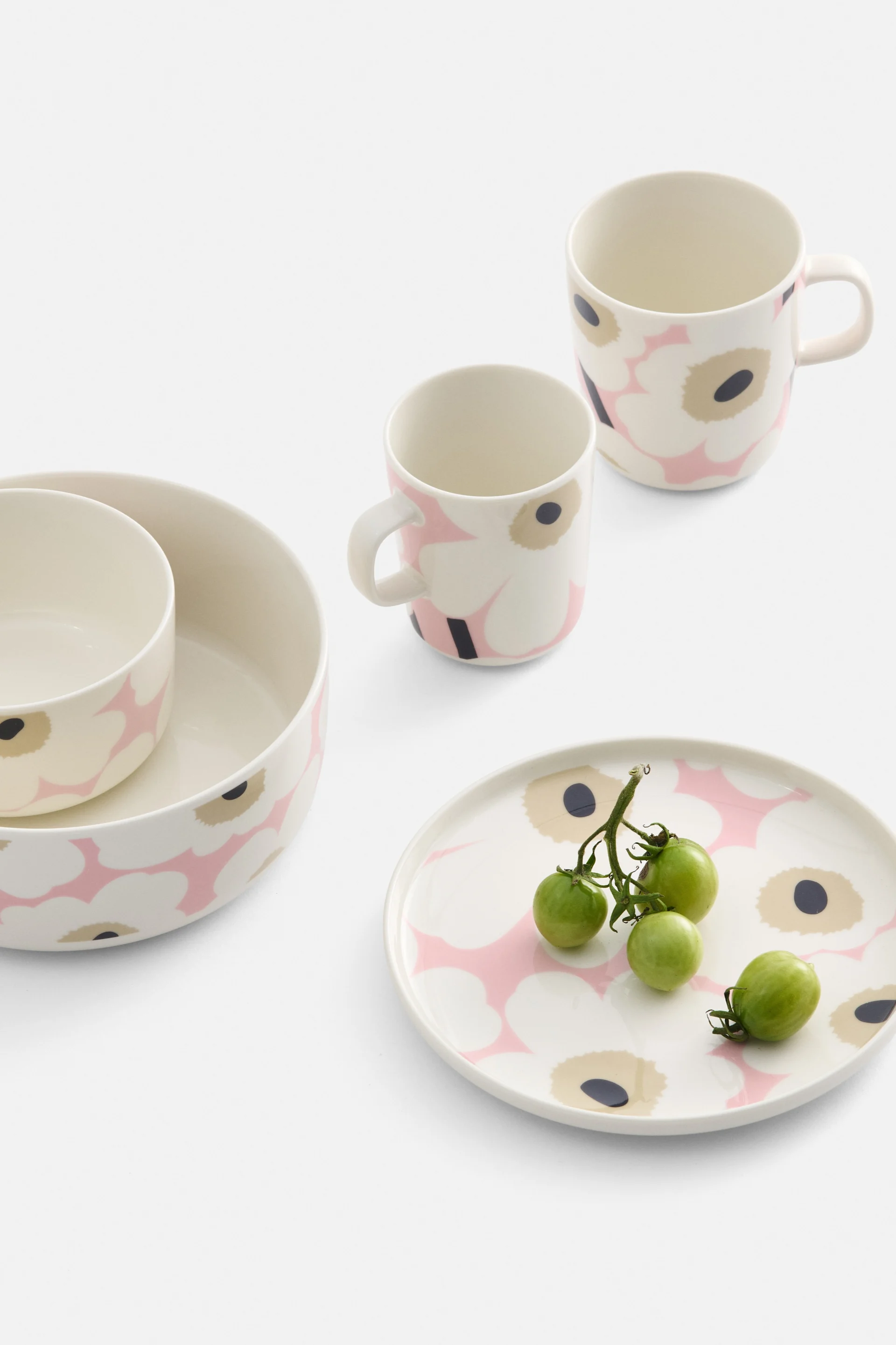 Vajilla de color crema con estampado floral rosa y negro, que incluye dos cuencos, dos tazas y un plato con tomates cherry verdes.