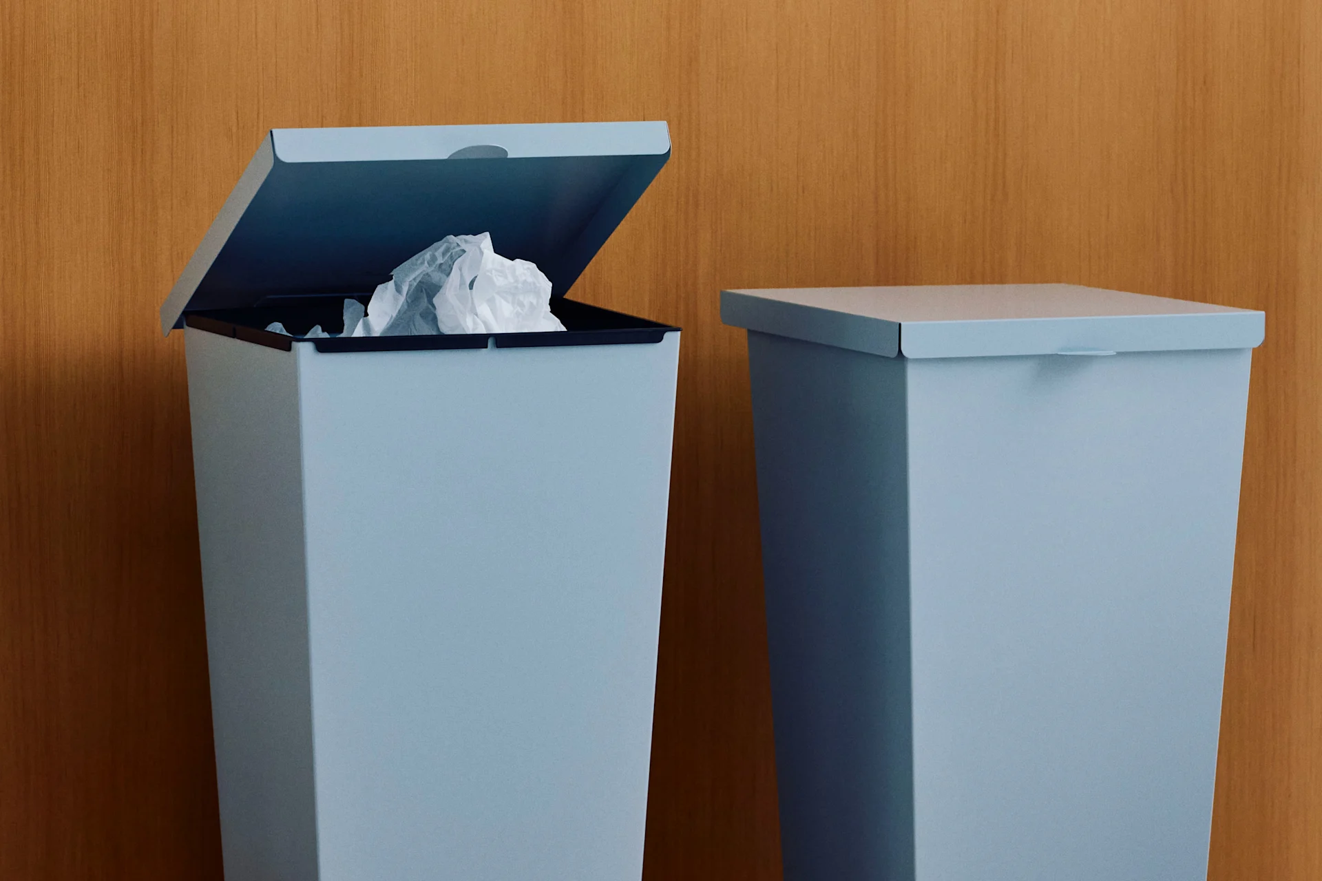 Dos papeleras azul claro contra una pared de madera, una abierta con papel arrugado.