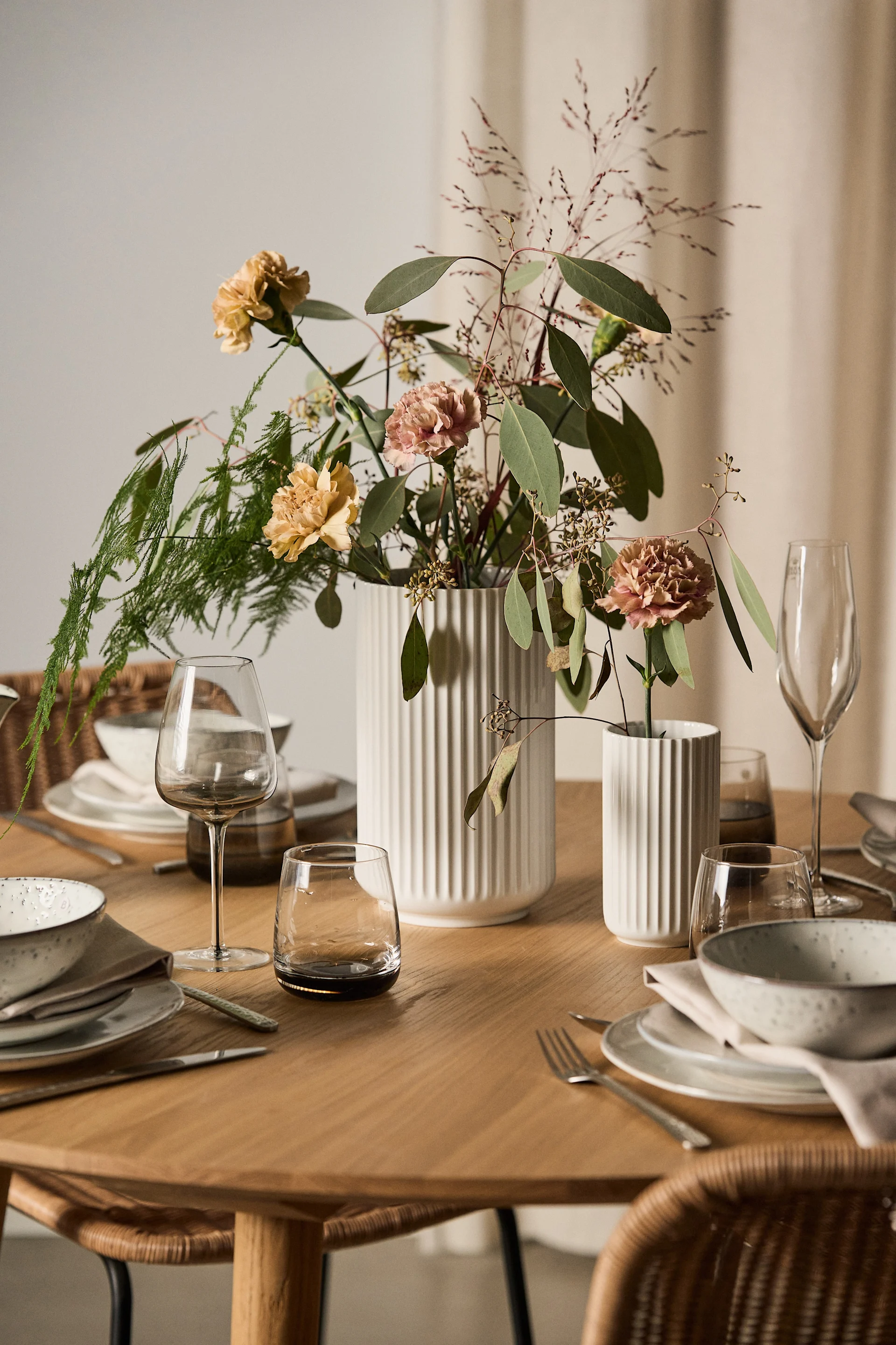 Un bonito regalo para el Día de San Valentín son las flores con un jarrón a juego. Aquí se muestran dos jarrones Lyngby en blanco con flores sobre una mesa puesta.