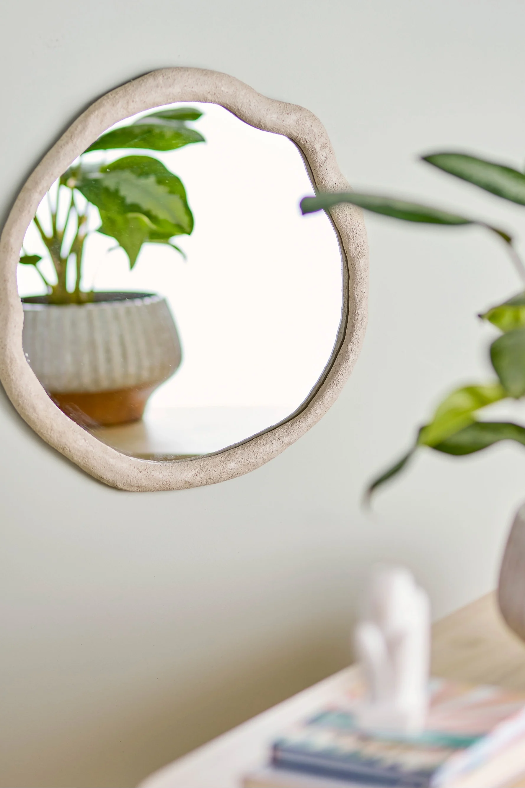 Decoración boho: el espejo Cillia de Bloomingville cuelga de una pared con una planta en una maceta.