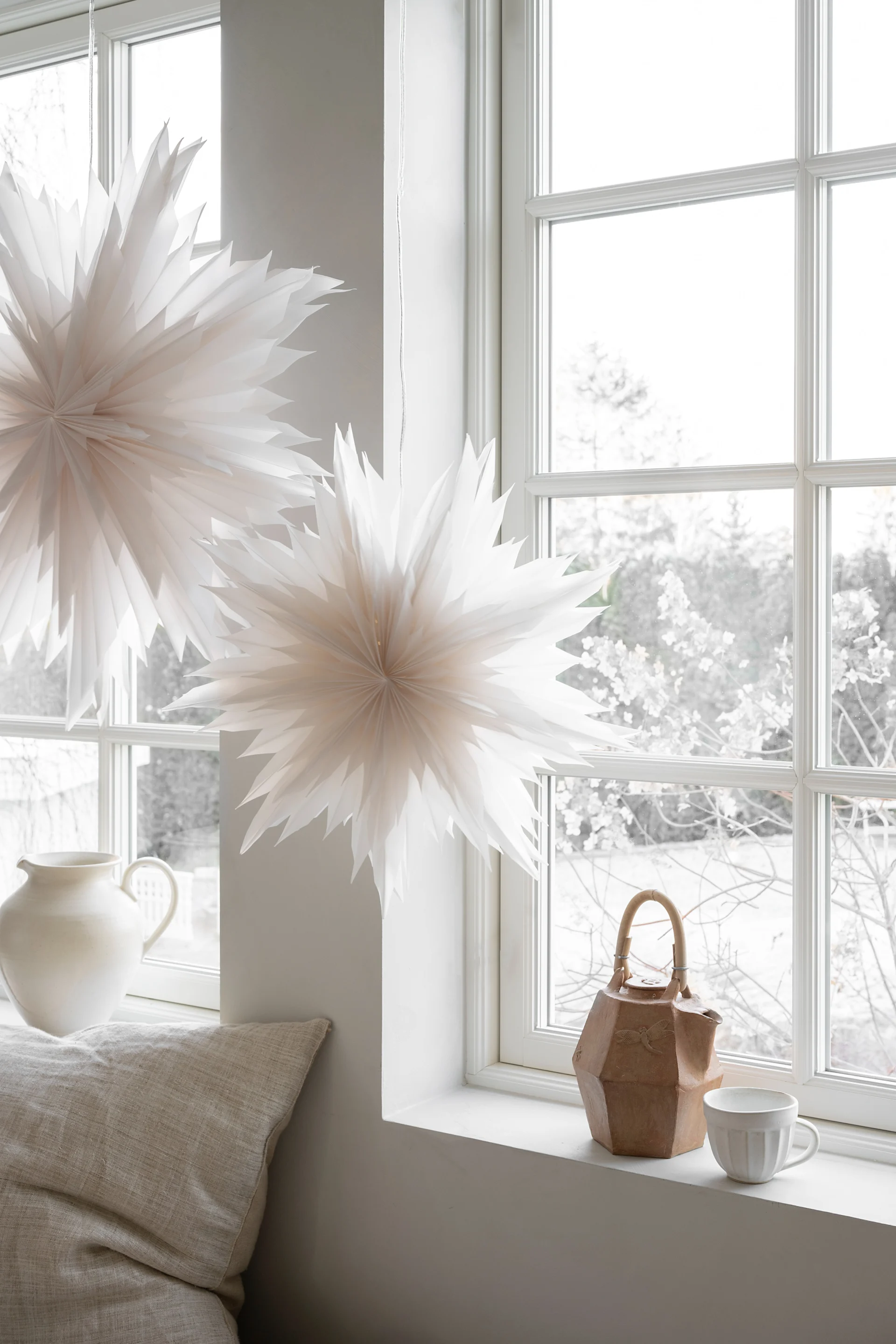 Estrellas de papel decorativas y adornos florales en capas exhibidos entre árboles de bosque cubiertos de musgo.