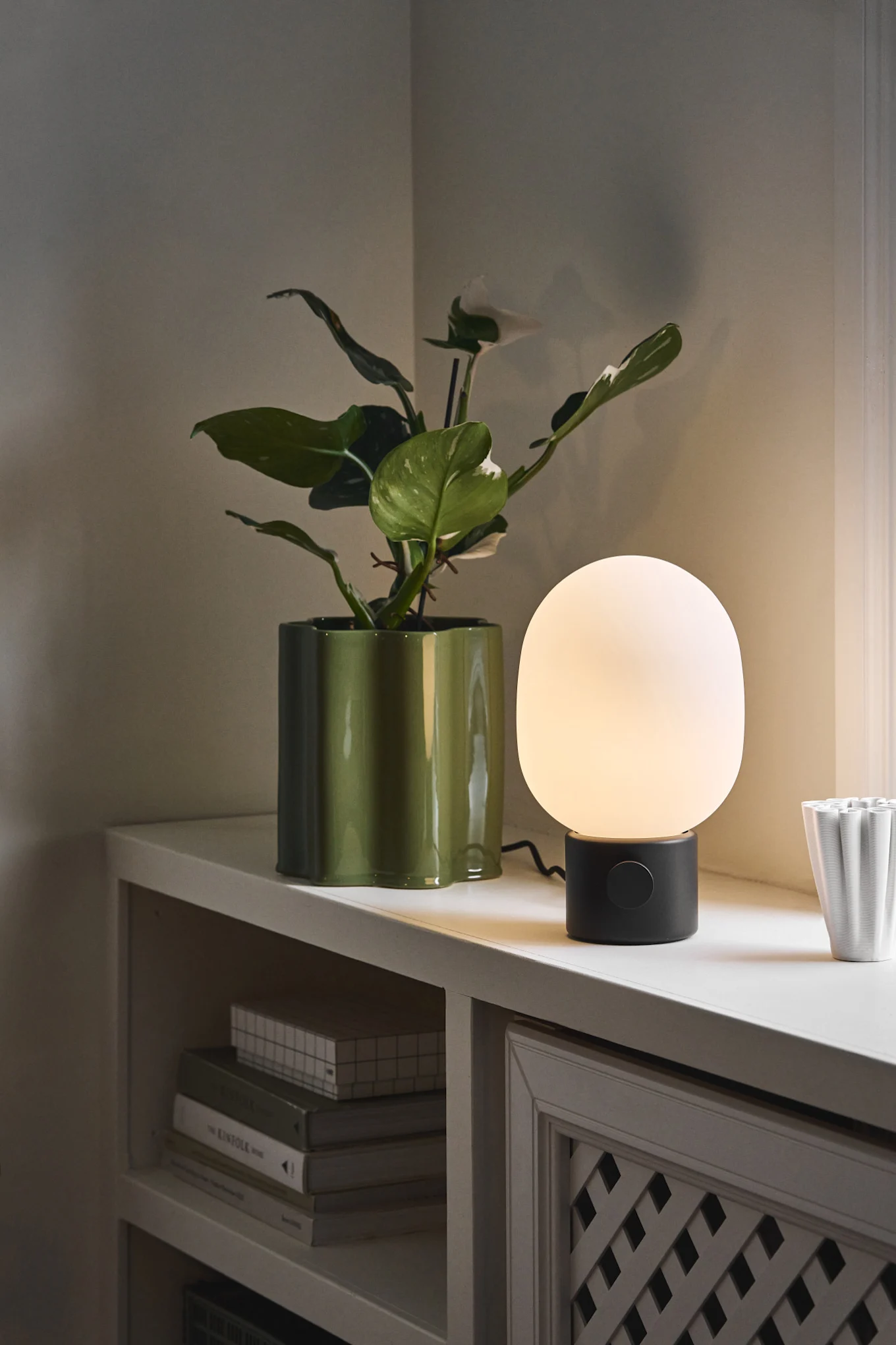 Lámparas escandinavas: la lámpara de mesa JWDA de Audo Copenhagen se encuentra junto a una maceta sobre un alféizar.