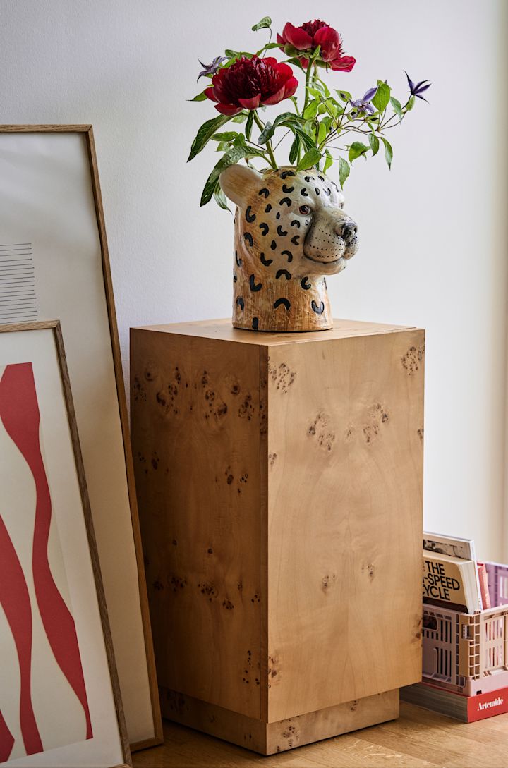 Uno de los productos más vendidos y emblemáticos de Byon es el jarrón Cheetah, un jarrón de guepardo que viene en dos tamaños diferentes. Aquí sobre un pedestal con un ramo dentro.