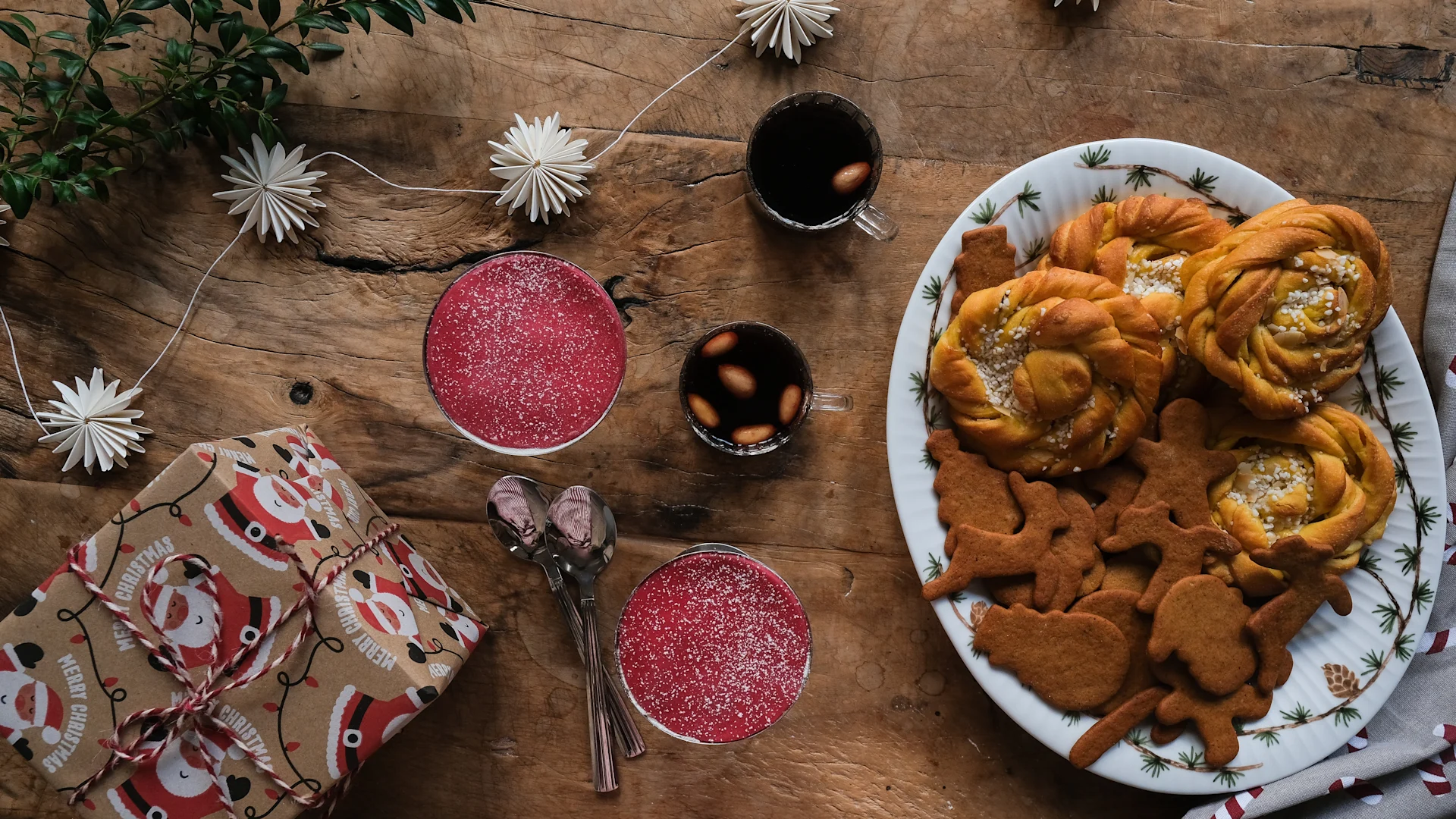 La gran fuente de Kähler, llena de repostería navideña, está sobre una mesa, junto al vino caliente, la tarta princesa en vasos y regalos.