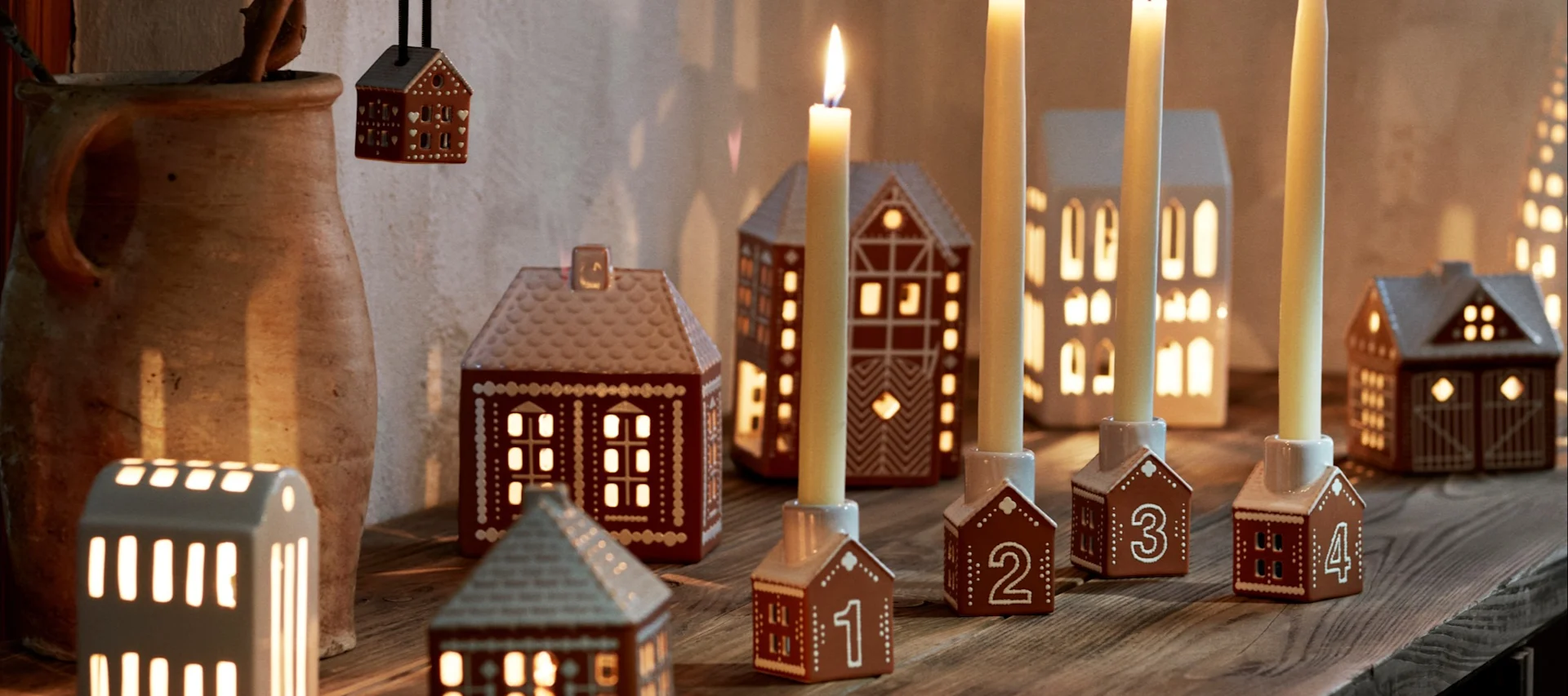Cómo decorar con adornos navideños tradicionales escandinavos: un niño pequeño con una casa de jengibre, rodeado de portavelas en el estilo de un pueblo de jengibre.