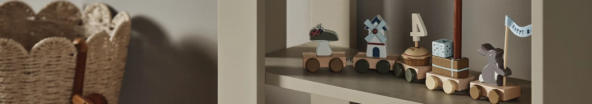 Un tren de juguete de madera en una estantería, con vagones que muestran una mariquita, molino de viento, cupcake con vela '4', regalo y un conejito con bandera "Happy B".