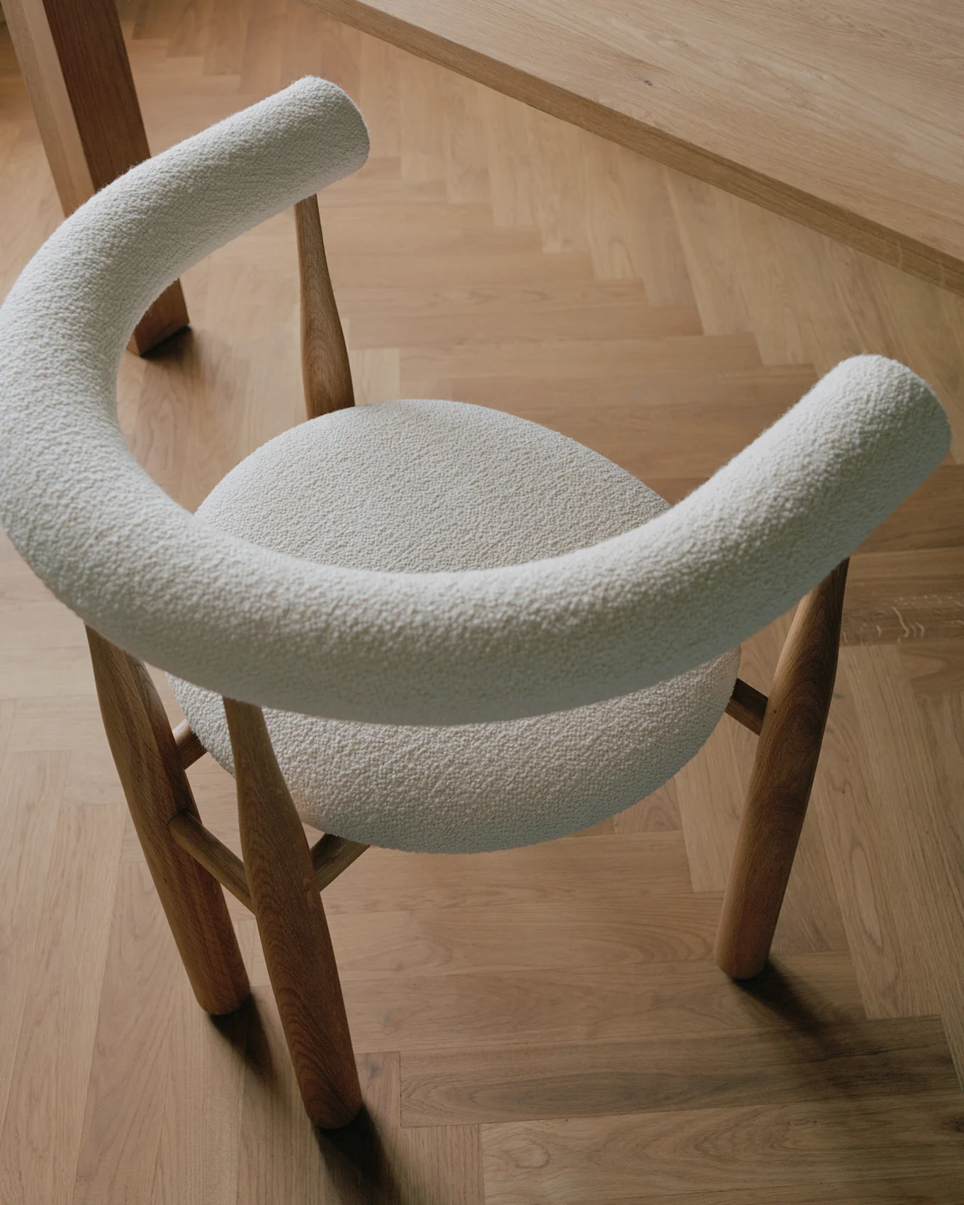 Silla moderna con tapicería bouclé crema claro y patas de madera, sobre un suelo de parqué de madera clara.