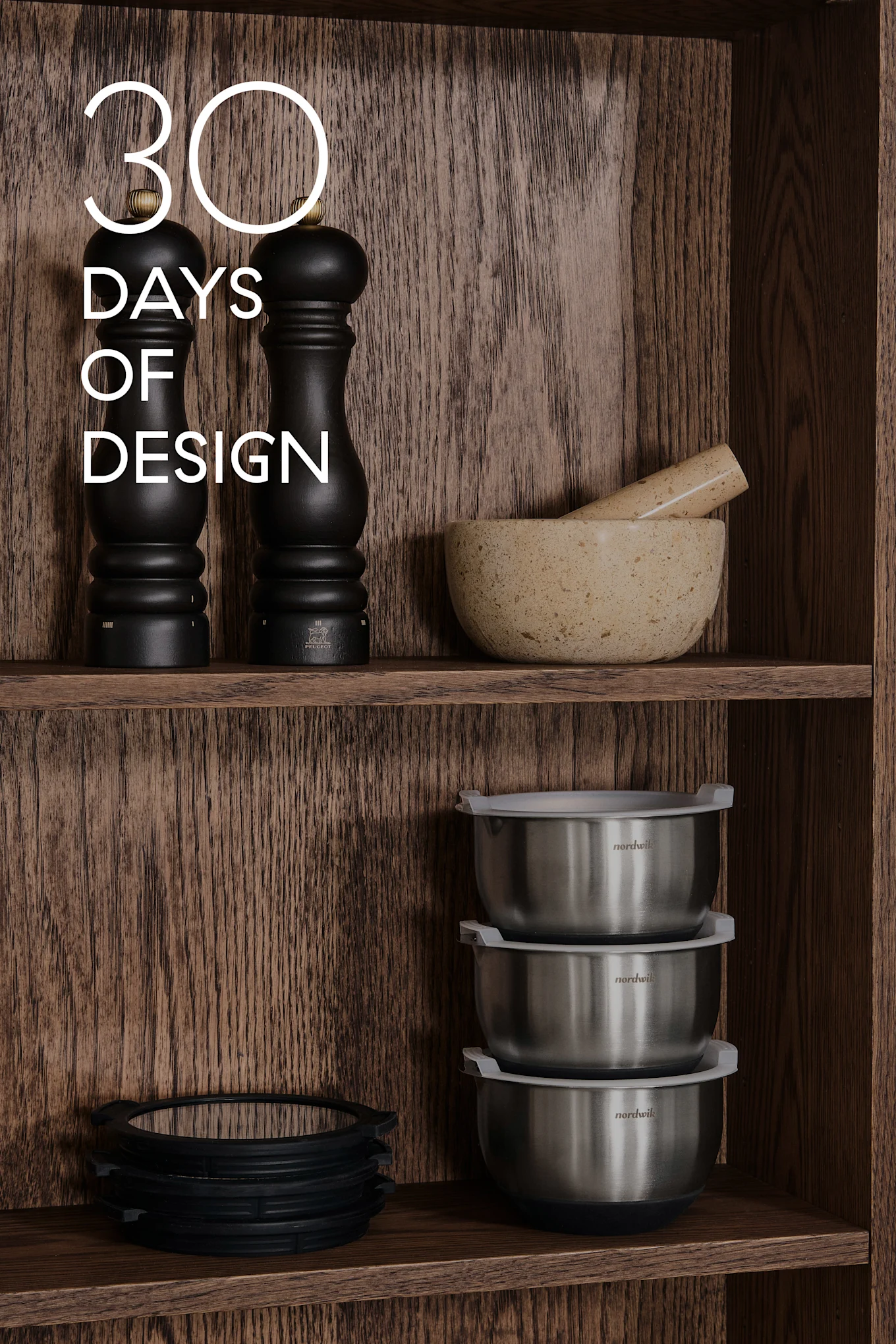 Estantes de madera con menaje: molinillos negros, mortero y mano, cuencos de acero, anillos de silicona. Texto: 30 DAYS OF DESIGN.