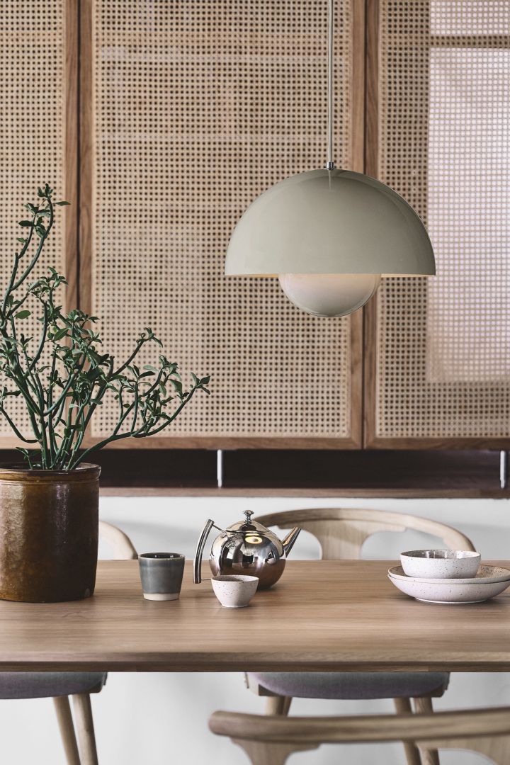 Disfruta de la tendencia Japandi con accesorios sencillos y claros como la lámpara colgante VP7 Flowerpot de &Tradition en beige, aquí la ves colgando en un entorno de comedor con una pared de ratán.