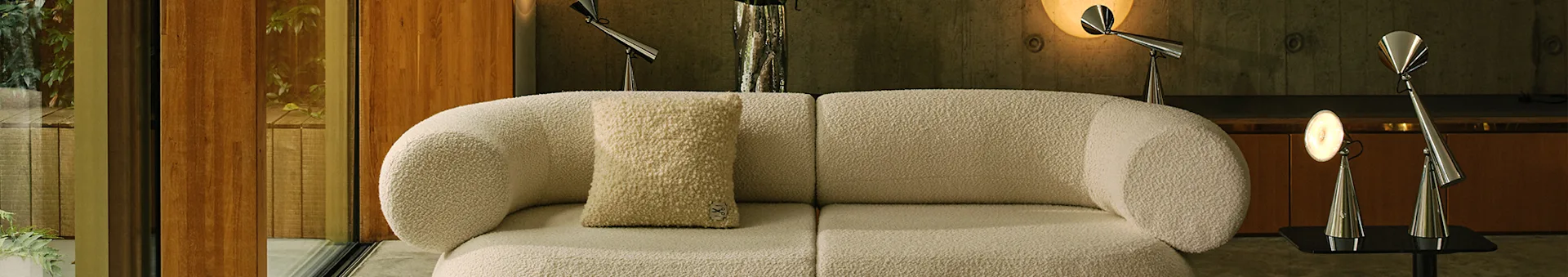 Sala de estar moderna con un sofá modular bouclé blanco roto, una alfombra clara estampada y lámparas de metal.