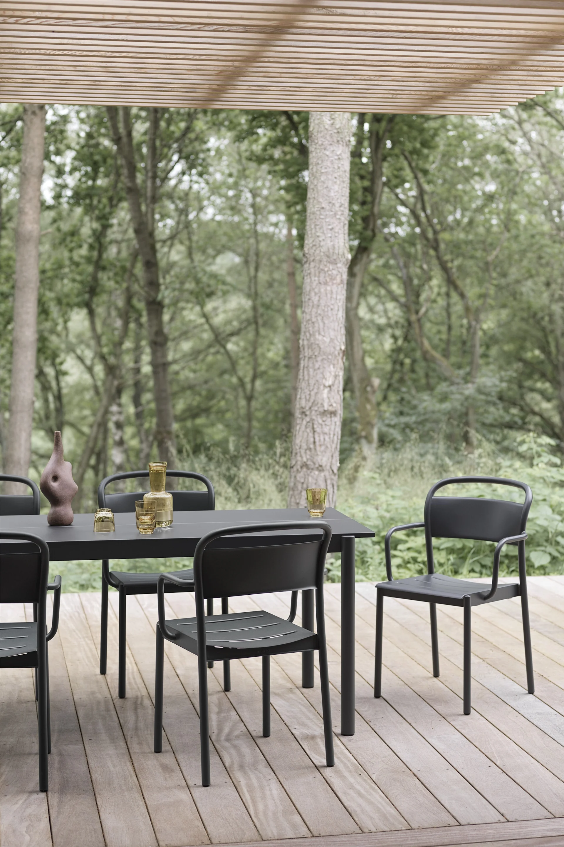 Una terraza cubierta de madera con una mesa y sillas negras de la colección Linear de Muuto.