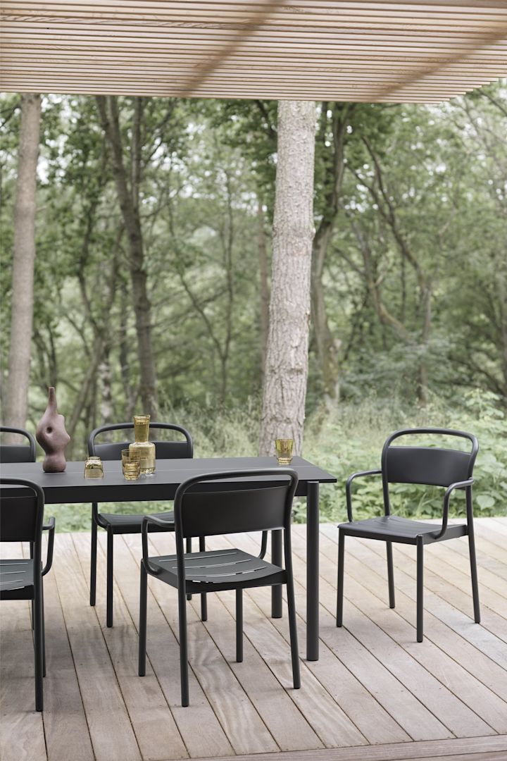 Una terraza cubierta de madera con una mesa y sillas negras de la colección Linear de Muuto.