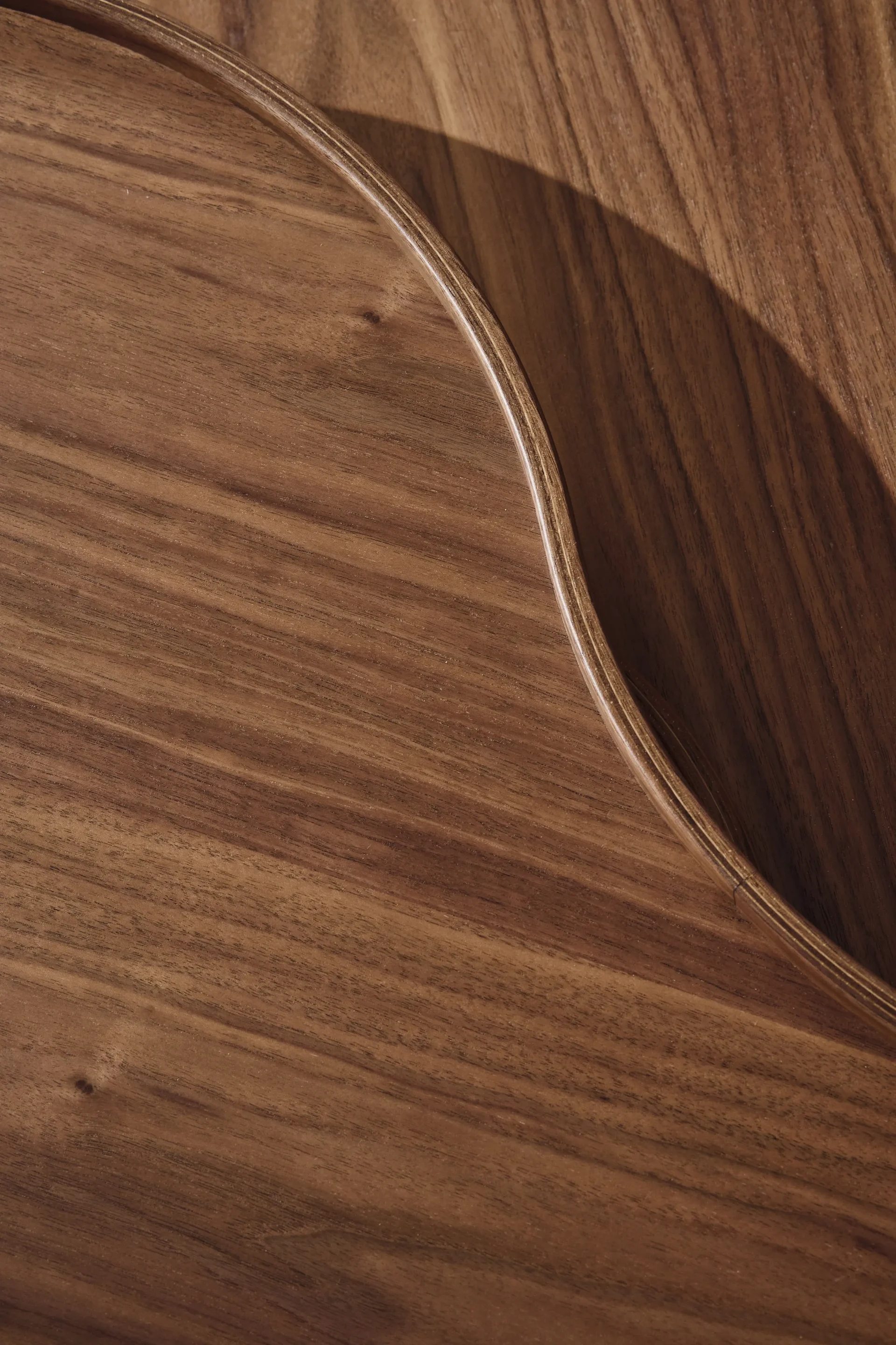 Primer plano de una superficie de madera marrón cálida con un borde curvo y elevado y vetas visibles.
