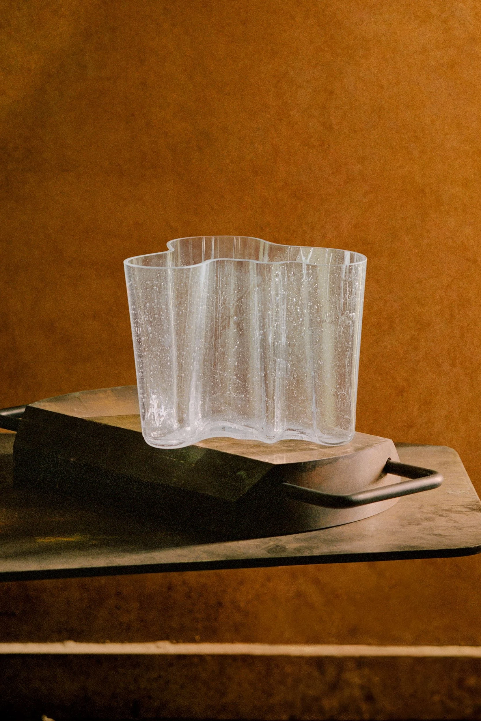 Jarrón de cristal transparente con forma ondulada y superficie texturizada, sobre una base de madera.