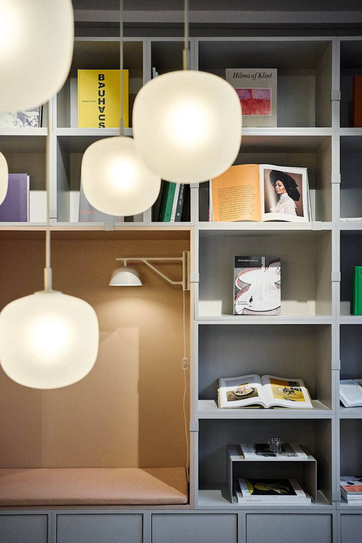 Una ordenada estantería decorada con libros, con varias lámparas de techo Rime de Muuto colgando en primer plano.