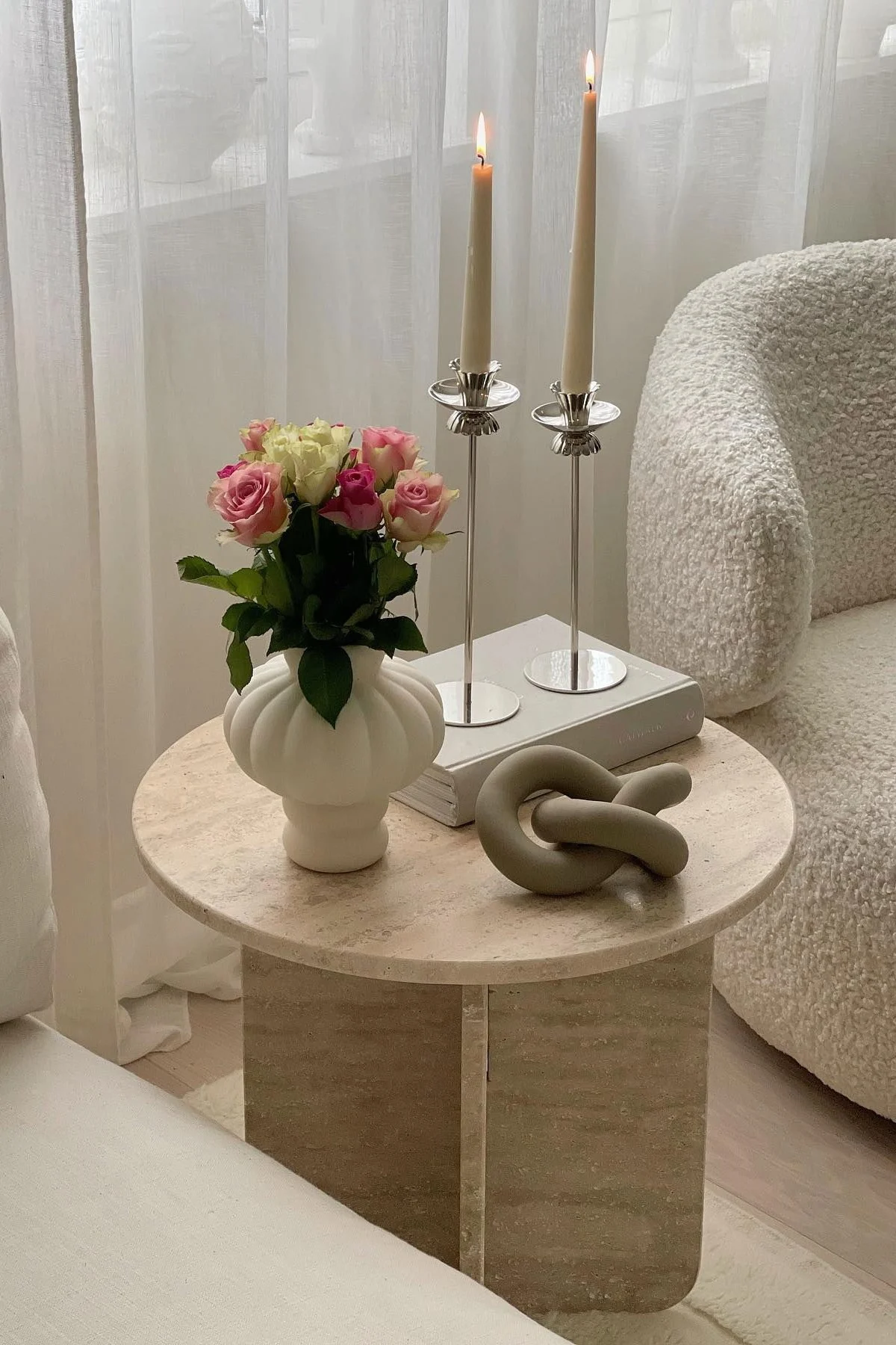 Un mesa de centro decorada con un jarrón Louise Roe Balloon, un libro, dos candelabros y la decoración Knot de Cooee Design.