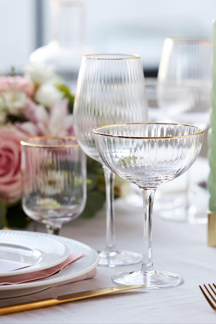 Los vasos de la colección Palermo de Lyngby Glas tienen un elegante borde dorado y se muestran aquí sobre una mesa puesta con estilo en blanco, rosa y dorado.