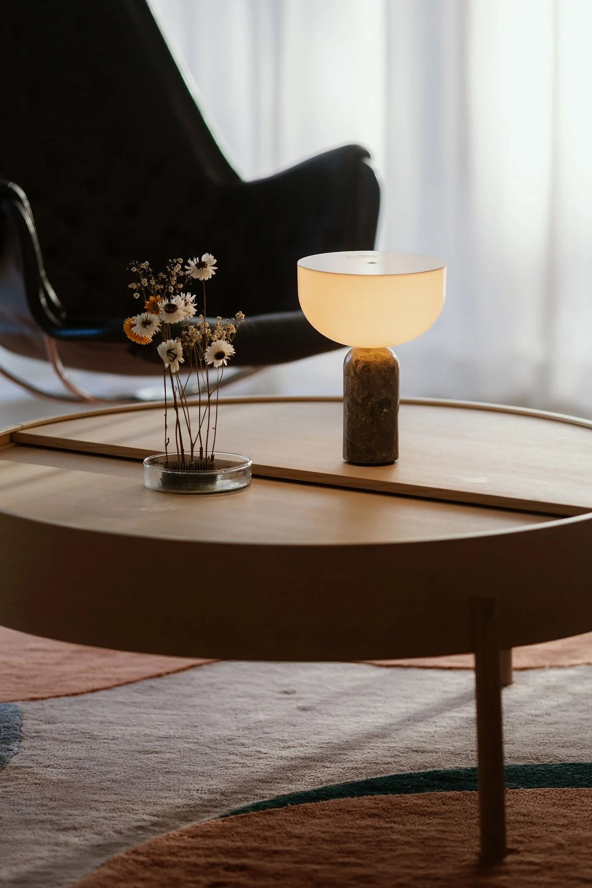 La mesa de centro Arc de Woud está decorada con una lámpara de mesa Kizu de New Works y el erizo de flores Garden Glory.