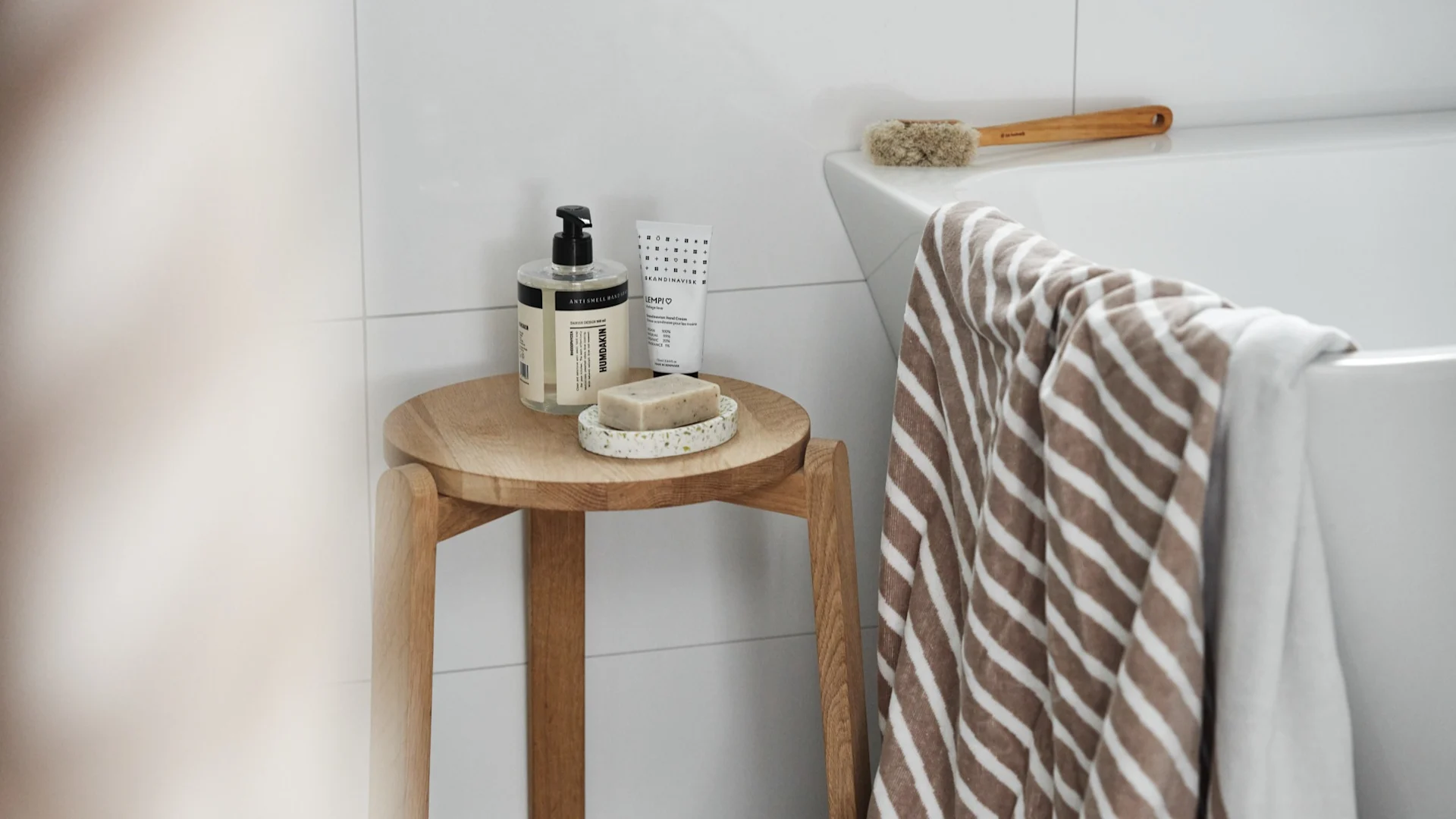 Regalo para el Día de San Valentín: organiza un día de spa y regala los utensilios necesarios. Aquí se muestra la toalla Stripes de NJRD colgada sobre una bañera, junto a un taburete con jabón y jabonera de Humdakin.