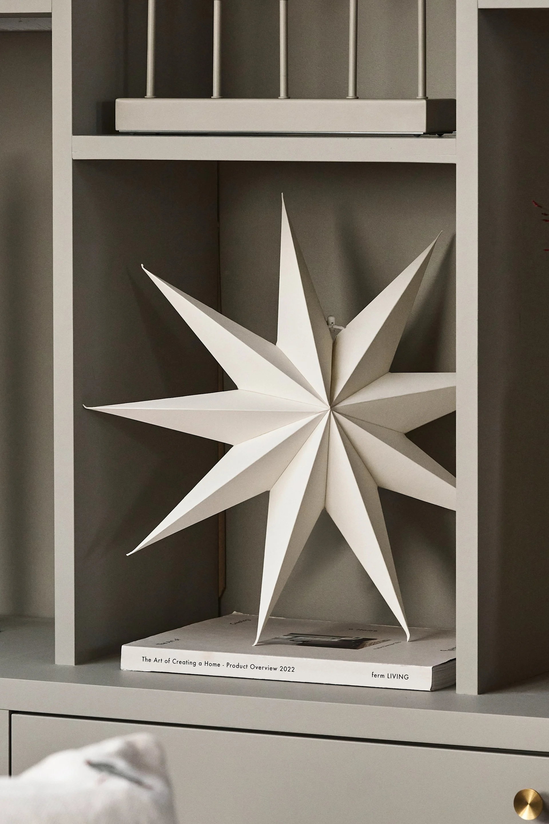 El farolillo de estrella de papel para Navidad – Venja – de Broste Copenhagen cuelga en la ventana junto a un par de candelabros y un jarrón.