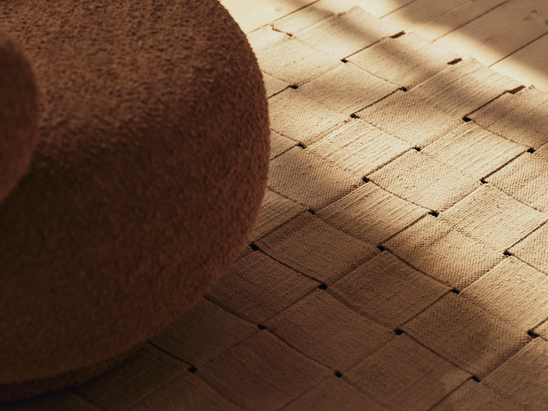 Muebles bouclé marrones, una alfombra tejida y un suelo de madera con sombras iluminadas por el sol.