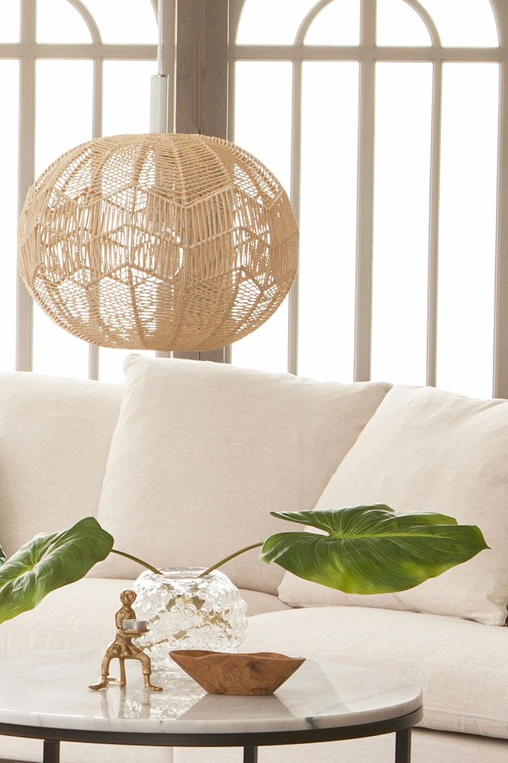 La lámpara colgante Missy de Globen Lighting hecha de ratán cuelga en un luminoso salón y es la decoración boho perfecta gracias a su material.