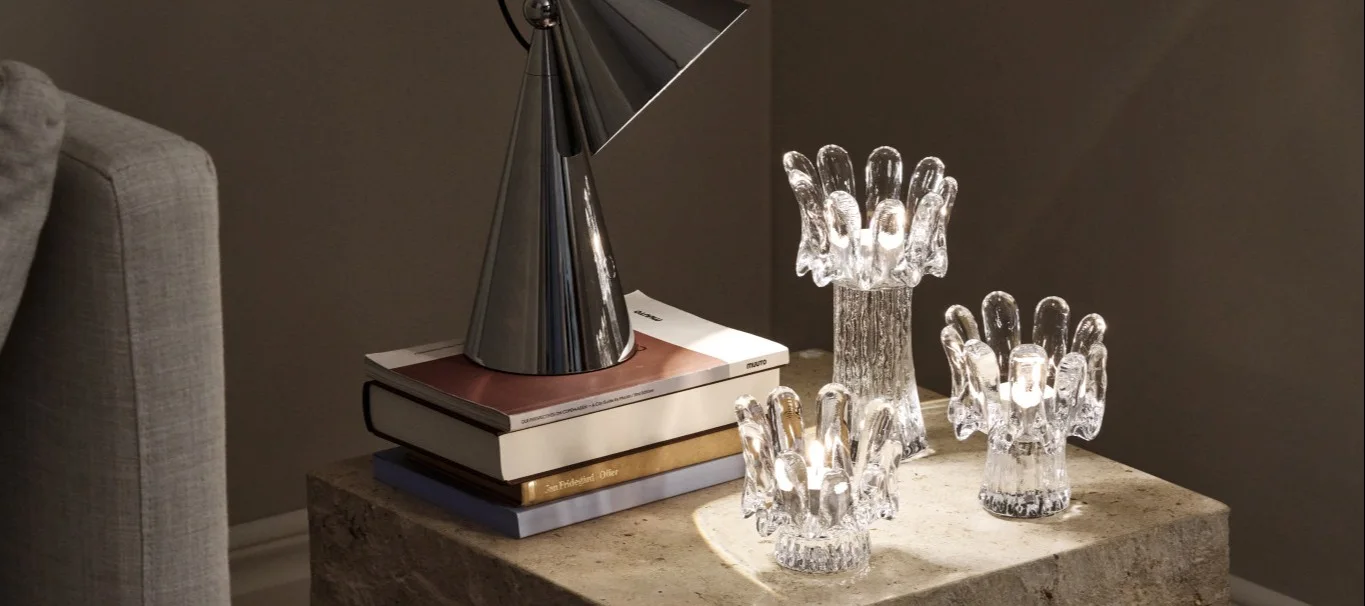 Tendencias de decoración 2026: sobre una mesita auxiliar de mármol hay una lámpara de mesa de Tom Dixon, que ilumina tres portavelas de cristal de la colección Solros de Kosta Boda.