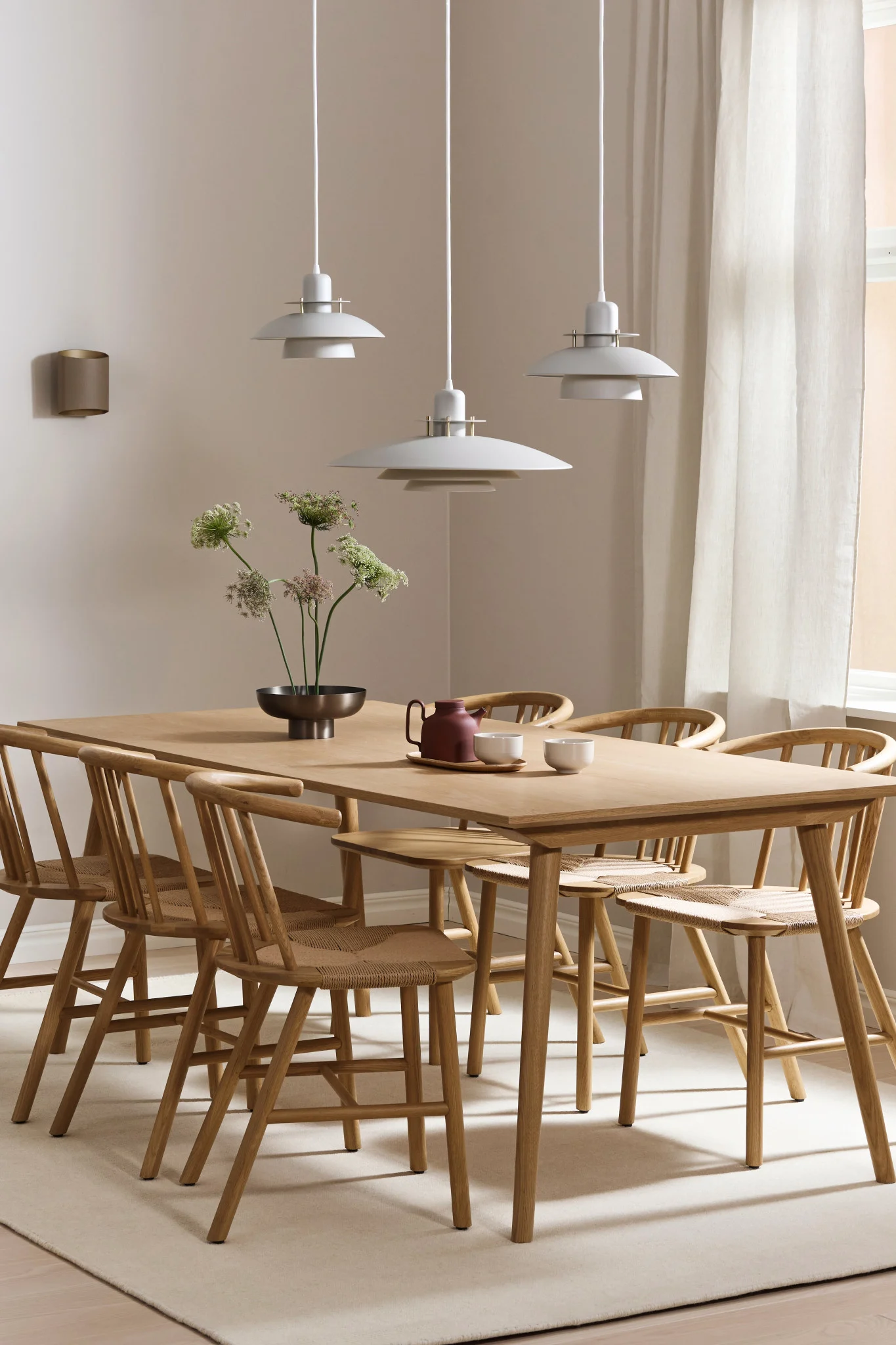 Aquí puedes ver ideas de iluminación de comedor para una mesa larga. La lámpara Picasso cuelga en una fila de tres y la lámpara Sinne cuelga de la pared.