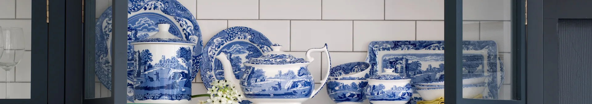Juego de vajilla de porcelana azul y blanca estampada con tetera, platos y cuencos en un gabinete azul oscuro.