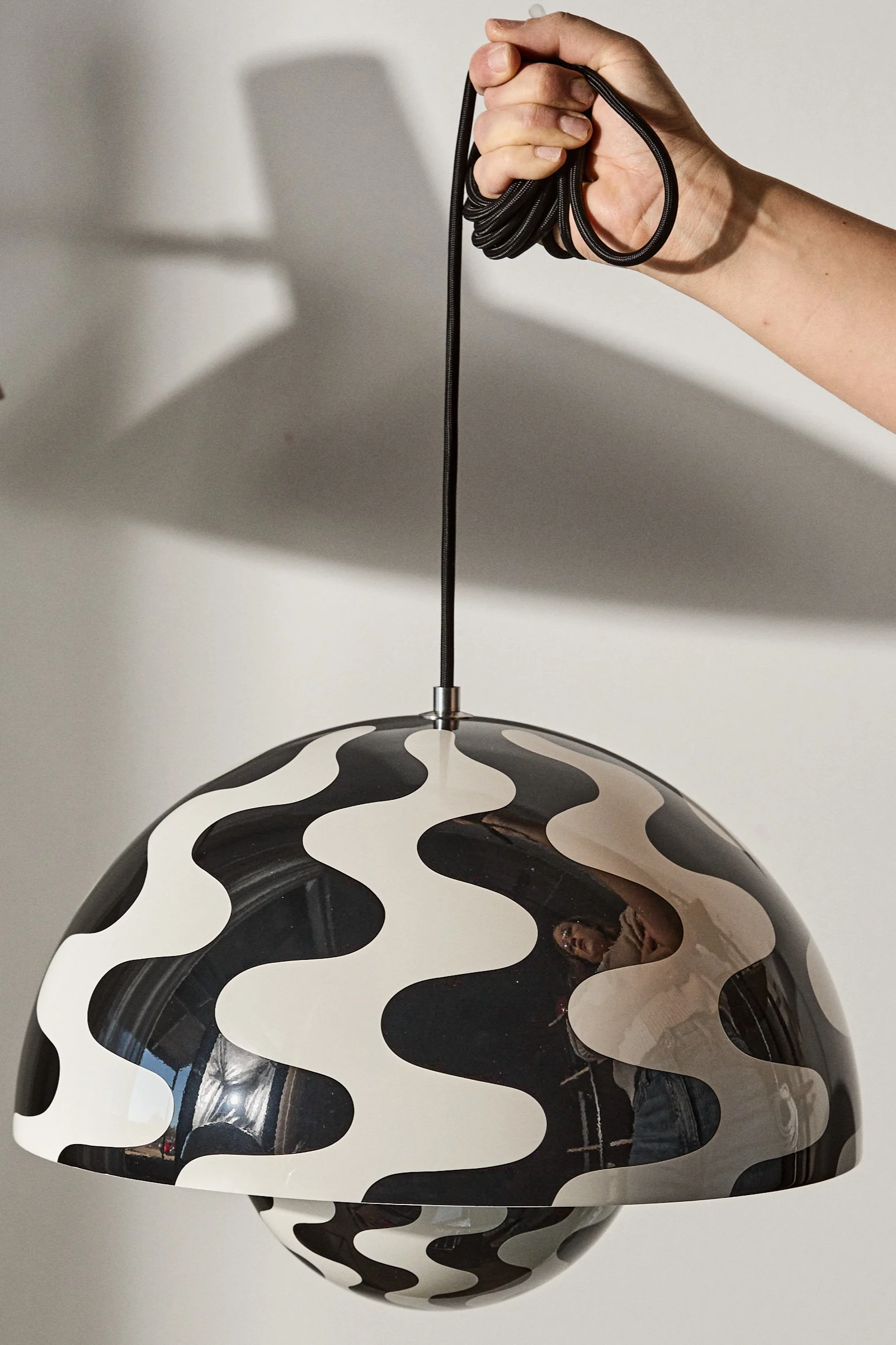 Las lámparas de techo con estampado para los salones pueden ser una forma divertida de decorar e iluminar. Aquí puedes ver una mano sujetando la lámpara de techo Flowerpot VP7 con motivos en blanco y negro.