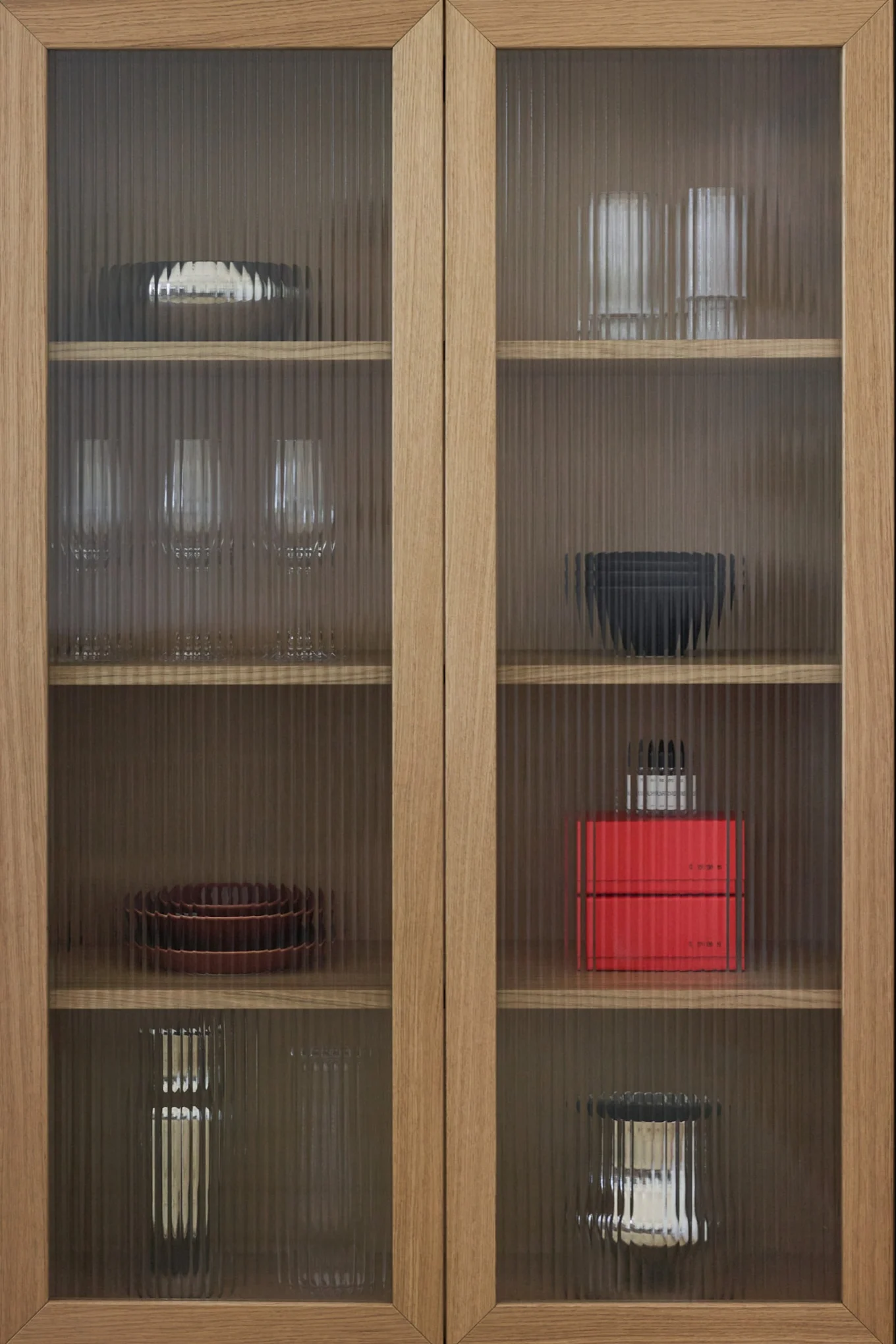 Armario de madera con puertas de cristal estriado, mostrando varios platos, vasos y objetos decorativos en estantes.