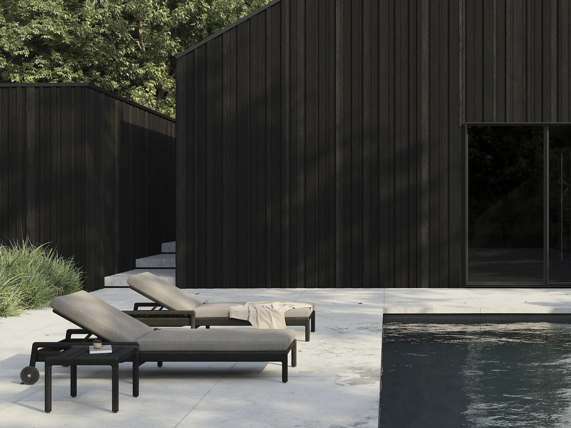 Dos tumbonas oscuras con cojines claros en un patio junto a una piscina, con edificios modernos de madera oscura al fondo.