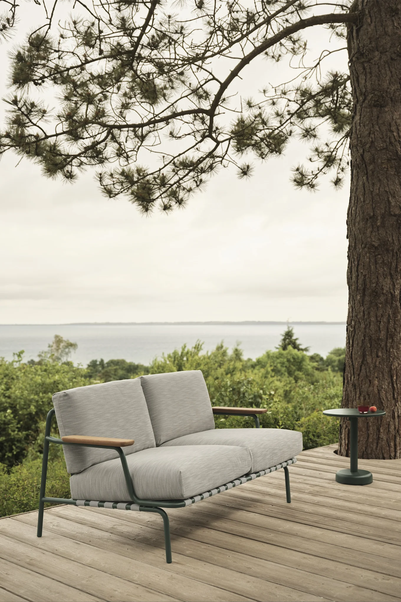 El sofá de exterior Settle de Muuto, mostrado aquí en una terraza con vistas al mar, ofrece espacio y, gracias a sus robustos cojines, un alto nivel de confort: un must-have entre las tendencias de mobiliario de jardín para 2025.