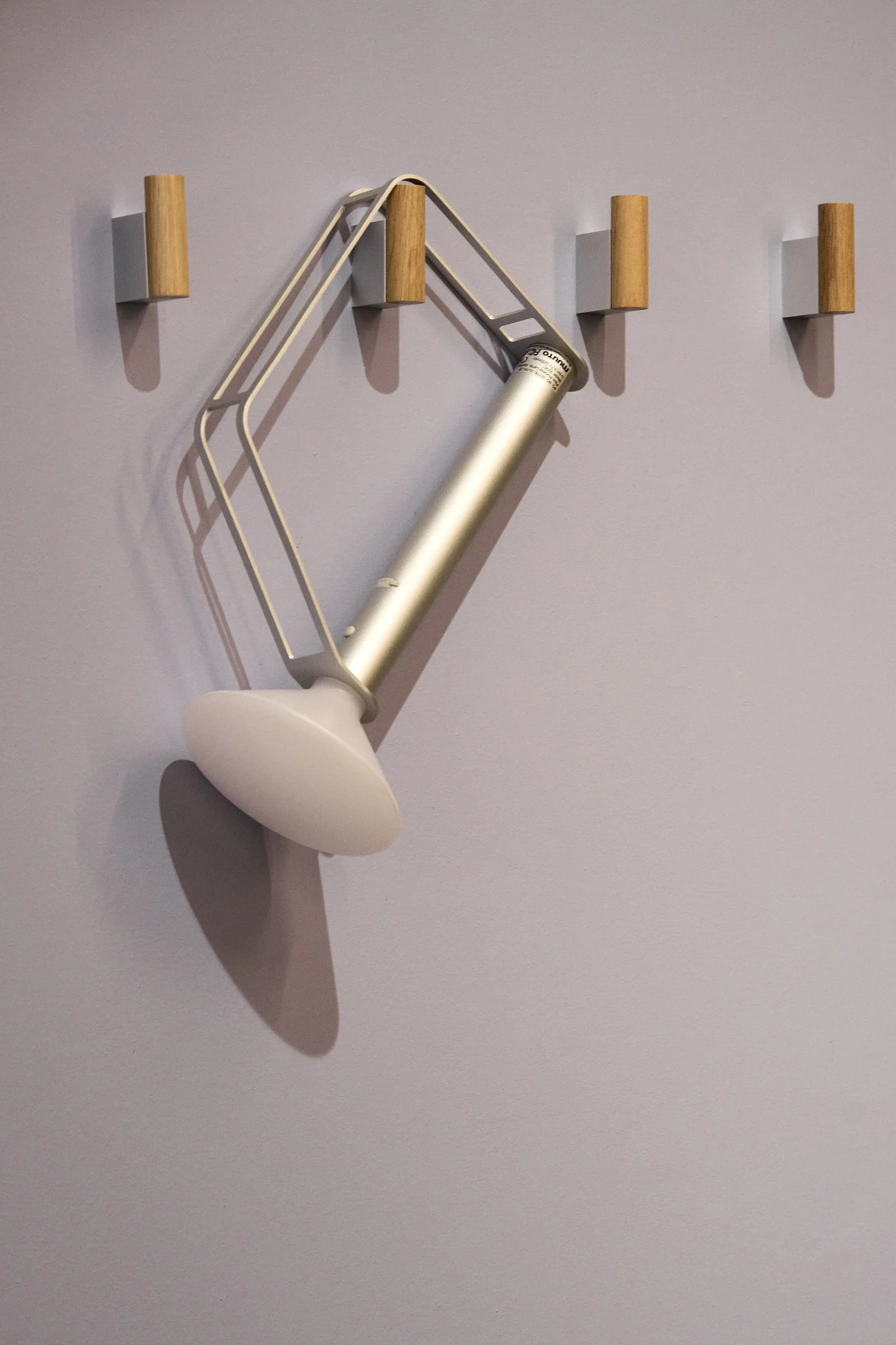 La lámpara de mesa Piton, plateada y portátil, de Muuto, cuelga de uno de los cuatro ganchos de la pared.