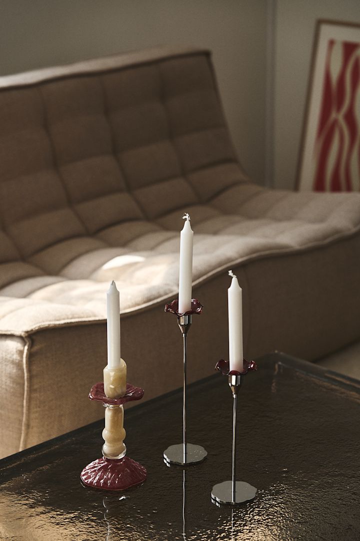 El candelabro Lara de Byon, aquí sobre una mesa de centro con tapa de cristal, está hecho de vidrio coloreado en beige y burdeos, el diseño está inspirado en las columnas romanas.