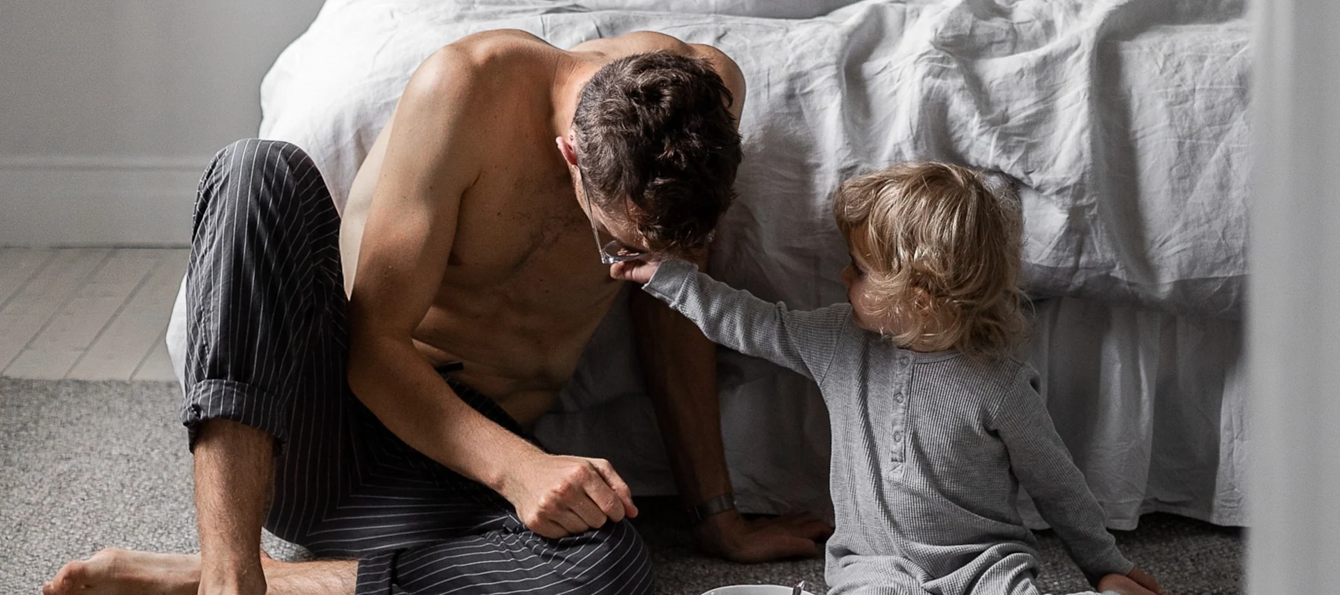 Aquí se ve a un hombre con un niño pequeño sentado frente a una cama.