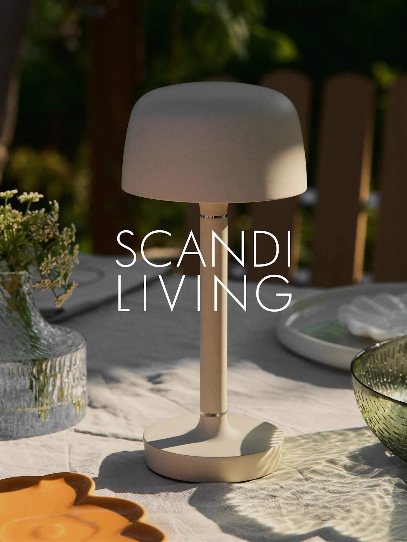 Lámpara de mesa portátil beige moderna en una mesa exterior con jarrón de flores y platos. Texto "SCANDI LIVING".