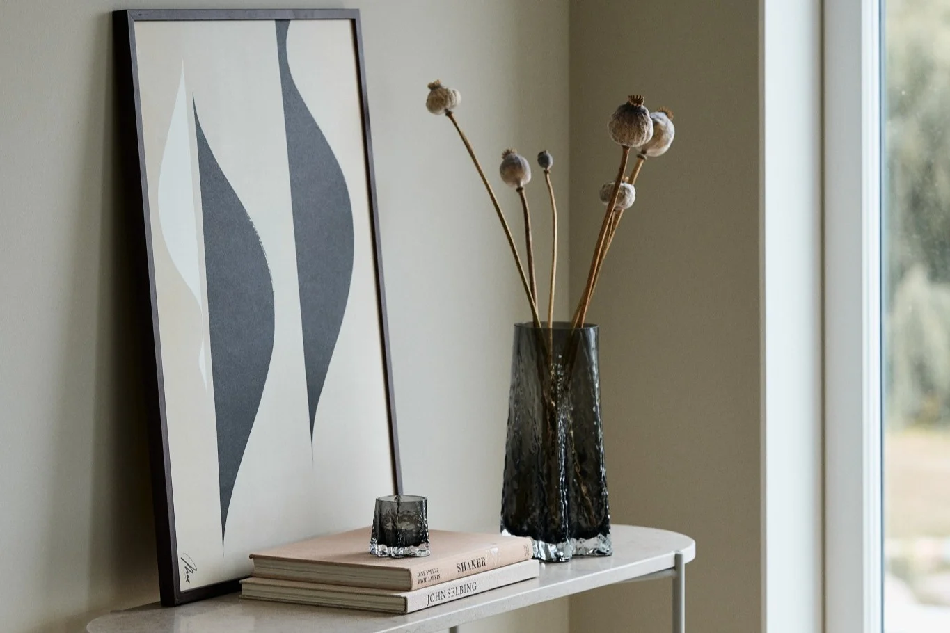 Aquí puedes ver el jarrón Gry de 30 cm y el candelabro Gry, ambos en color Smoke, de Cooee Design, sobre un aparador delante de un cuadro.