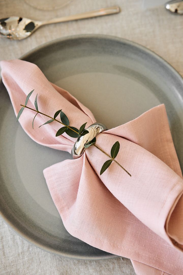 Decora la mesa de tu cena romántica en casa con colores agradables. Aquí puedes ver la servilleta Clean en Dusty Rose de Scandi Living sobre un plato con servilletero.