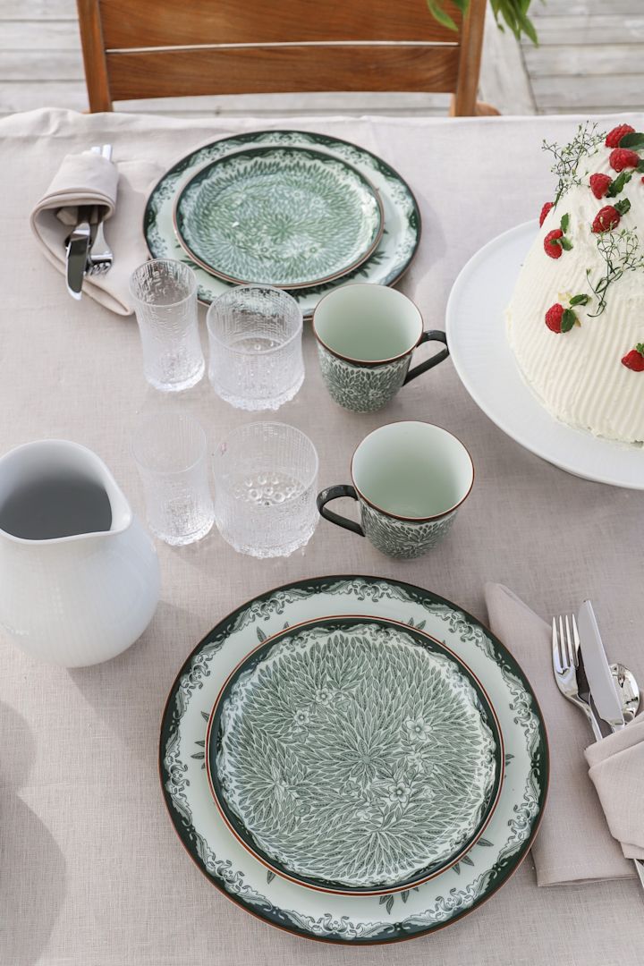 Entre las ideas tradicionales para las fiestas de verano figuran las cenas al aire libre. Aquí puedes ver las series Ostindia verde y Ostindia Floris sobre la mesa con los vasos ultima thule de Iittala.