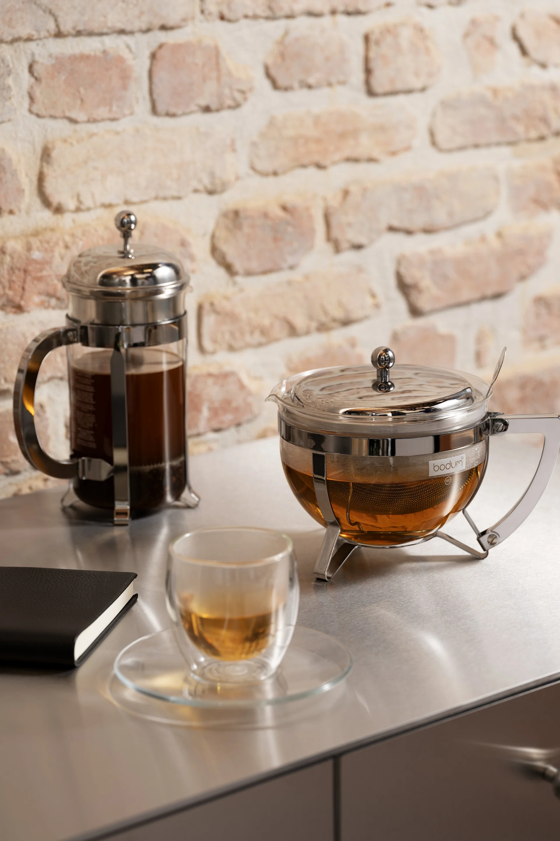 Regalo para el Día de San Valentín: aquí se muestran una prensa francesa y una tetera de la colección Chambord de Bodum, junto a una taza tipo bistró con té sobre una encimera de cocina.