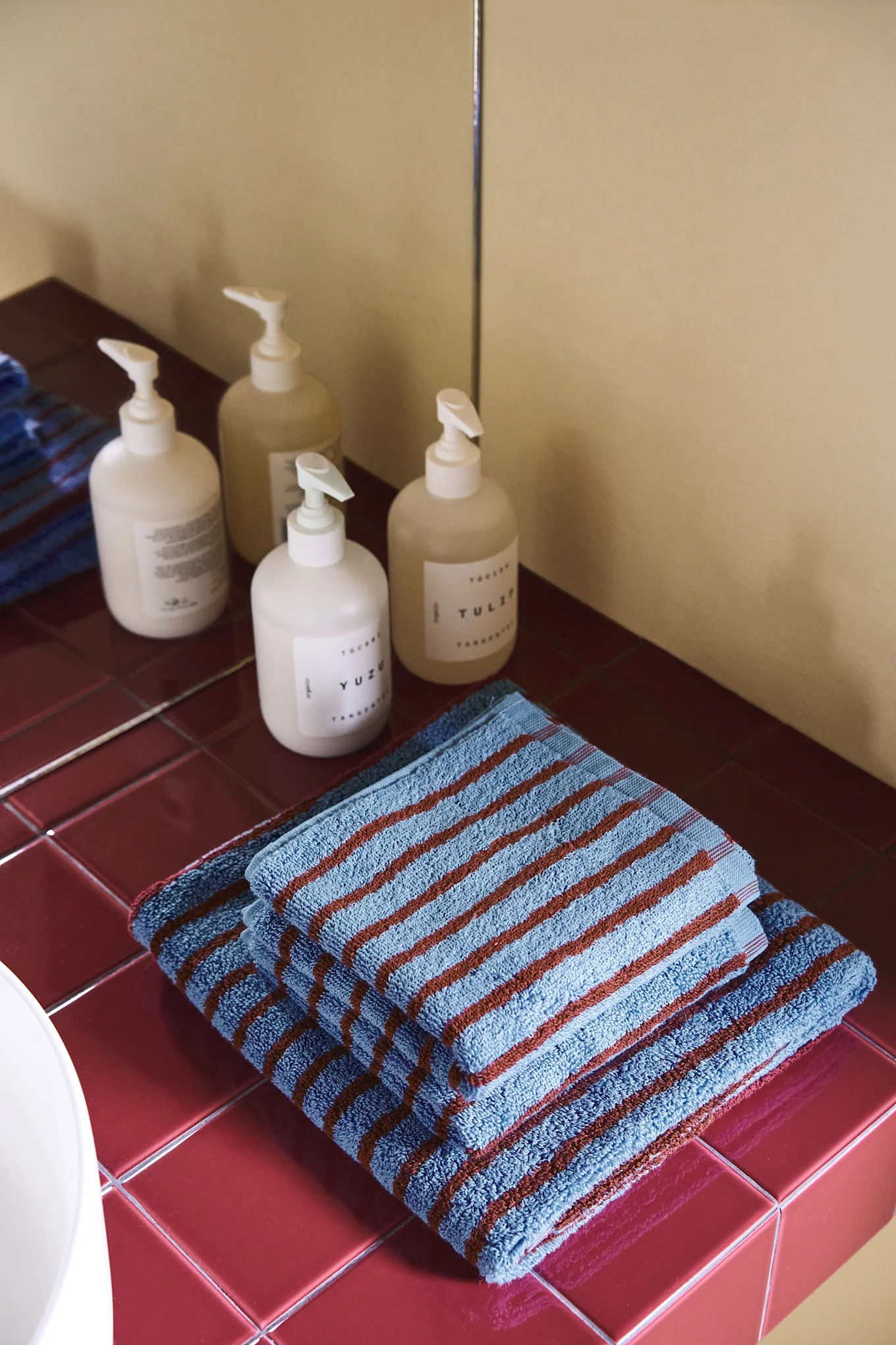 Encimera de baño con cuatro botellas dispensadoras y dos toallas azules con rayas marrones sobre azulejos rojos.