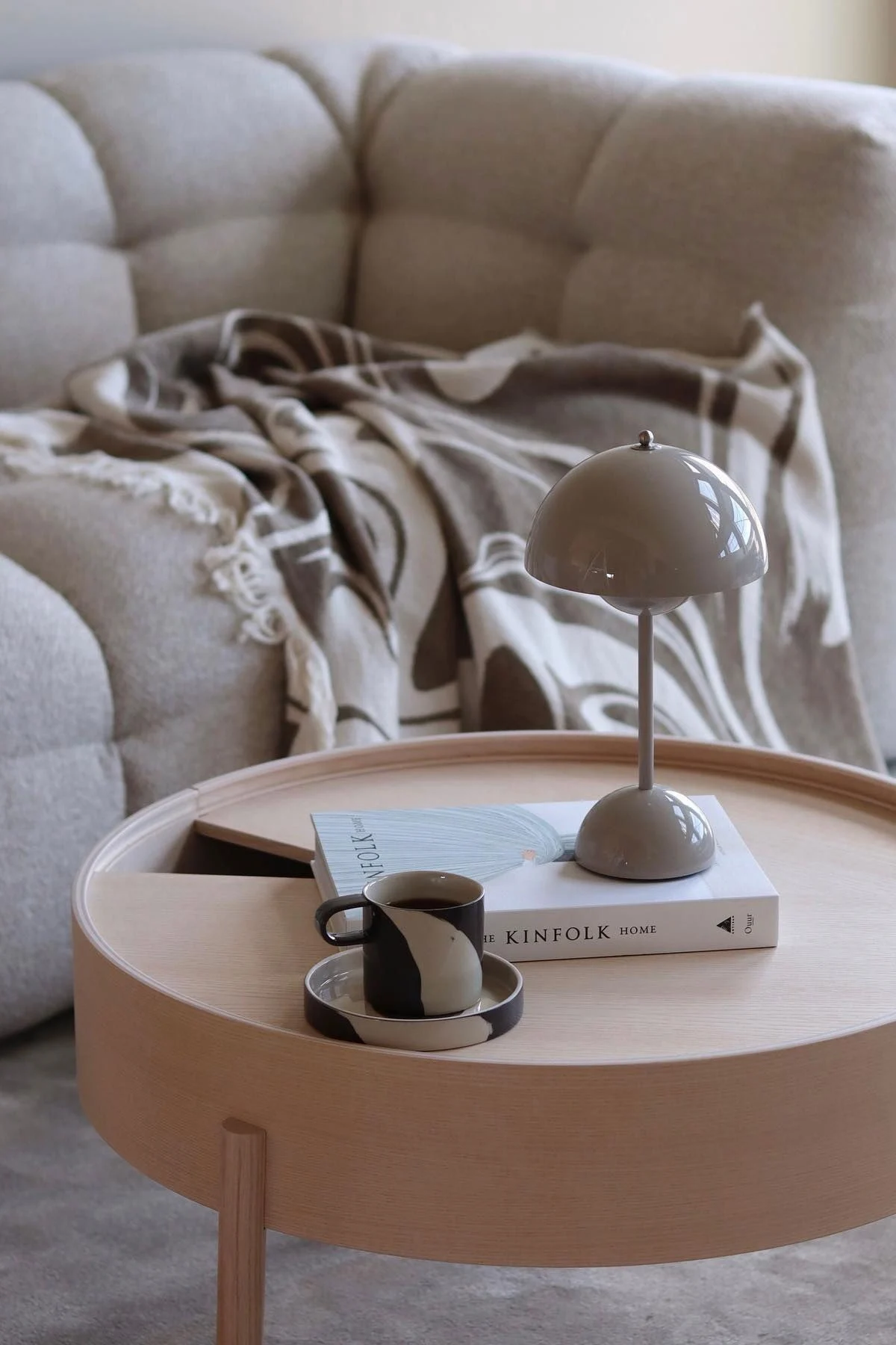 Una mesa de centro de madera está decorada con un libro, una lámpara de mesa Flowerpot de &Tradition y la taza Inlay de Ferm Living.