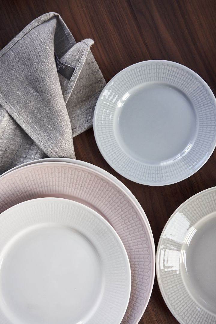 Platos Swedish Grace en blanco, rosa, azul y gris sobre una mesa de madera oscura.