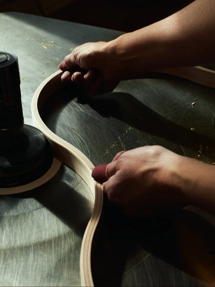 Manos lijando una tira de madera curvada en una máquina de taller.