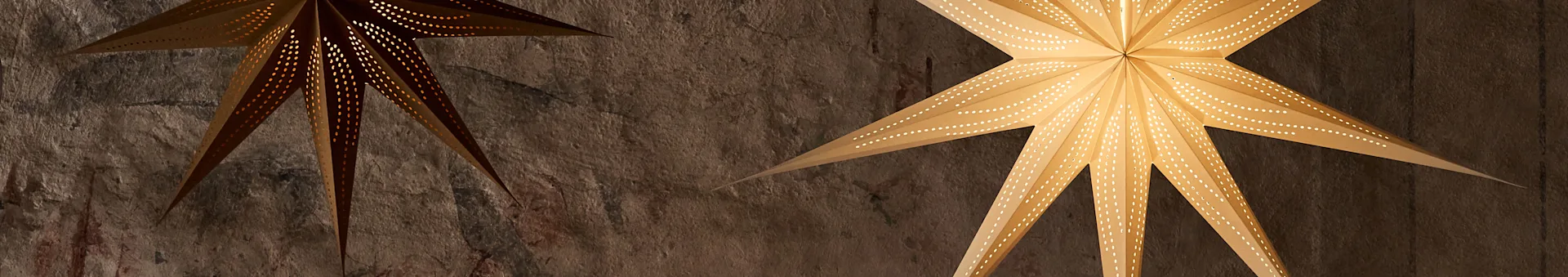 Dos farolillos de papel en forma de estrella iluminados con patrones de puntos perforados, colgando contra una pared texturizada.
