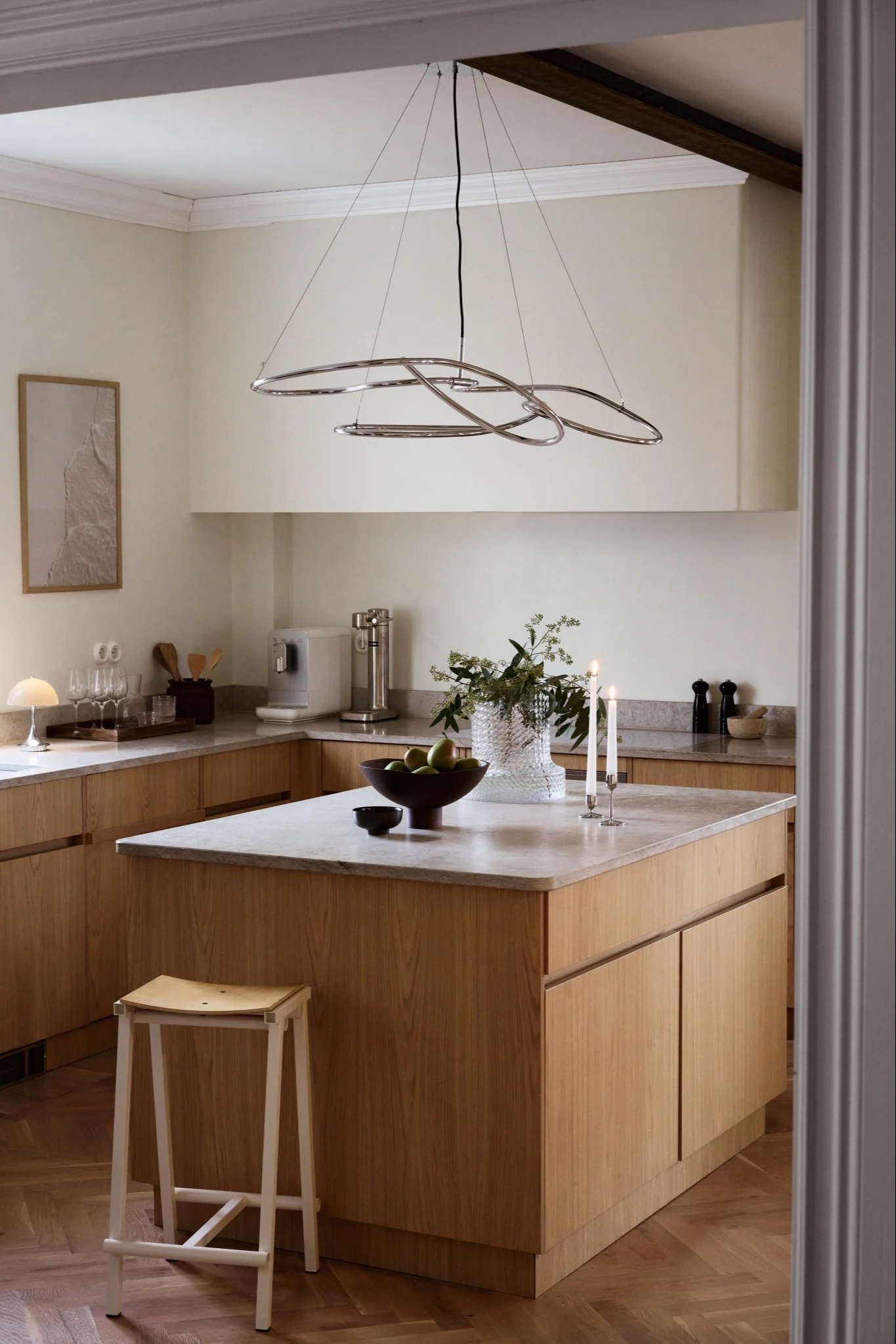 Cocina moderna con gabinetes de madera clara, encimeras de mármol, una isla grande y una lámpara de cromo escultural.