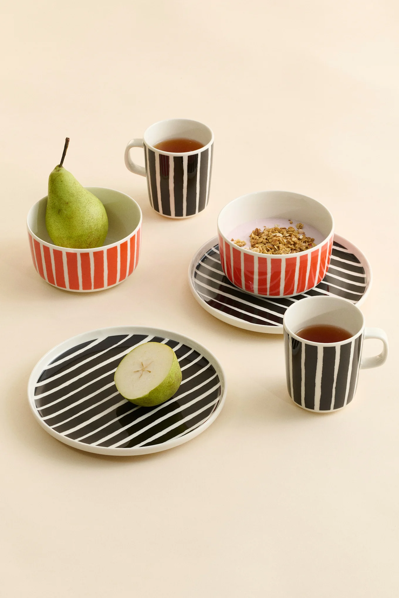 Tazas de cerámica a rayas con té, cuencos con una pera y yogur con granola, y platos con media pera.