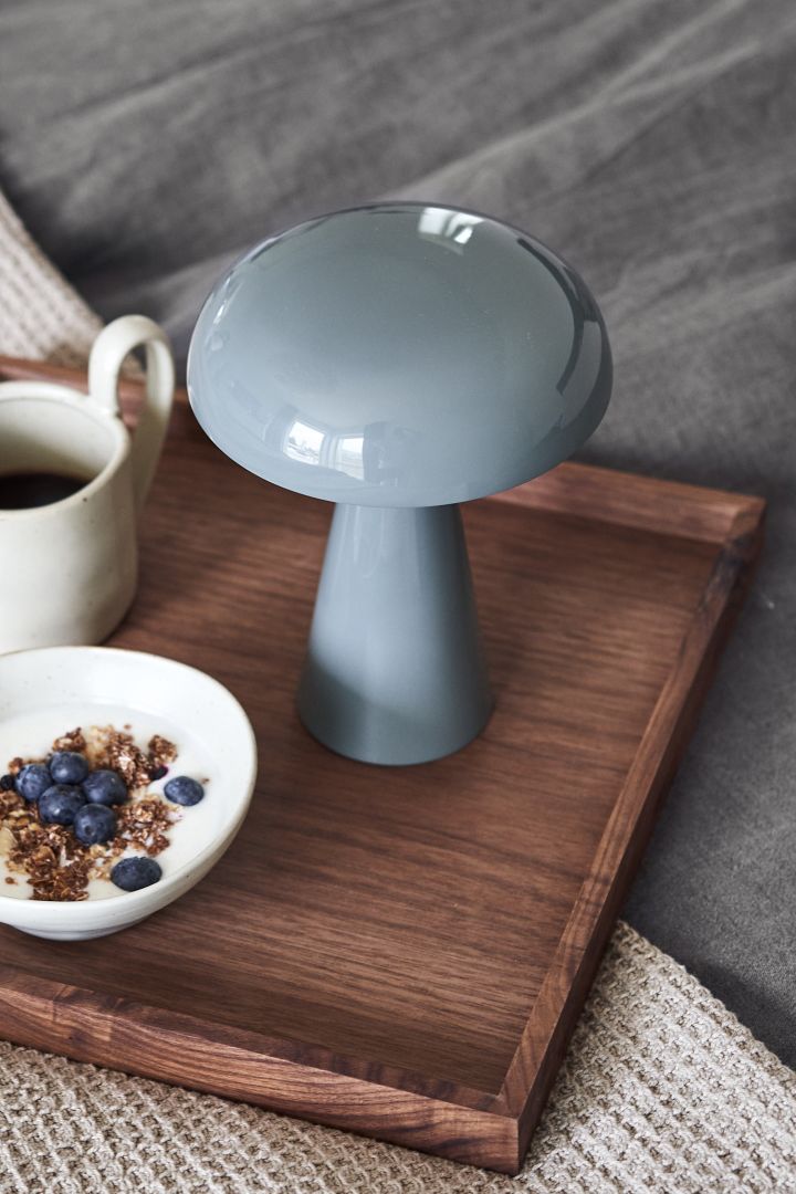 La lámpara portátil e inalámbrica Como en azul piedra de &tradition sobre una bandeja de desayuno. 