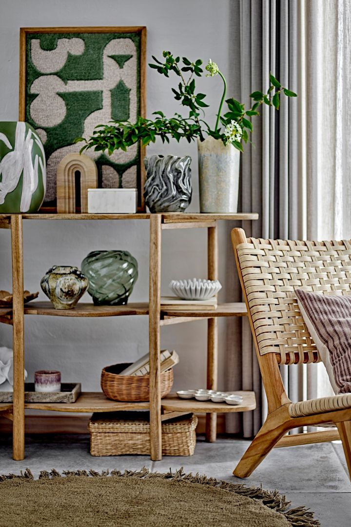 Un salón amueblado en estilo boho con un sillón, una estantería decorada y la decoración mural Longton de Bloomingville.